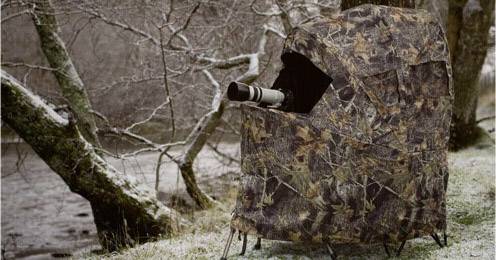 Egy rejtőzködő berendezés az erdő szélén, amely elrejti a fotóst, miközben egy kamera kiáll, hogy vadvilág-fotókat készítsen a természetben.