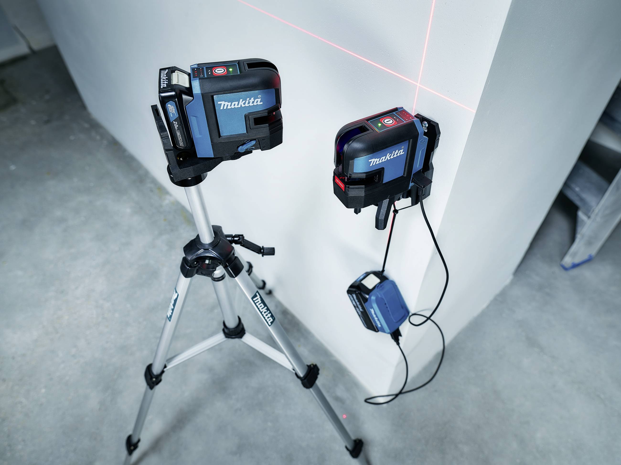 Két kék lézer szintező eszköz, egyik állványon, másik a falon rögzítve, piros vonalakat vetít egy fehér falra.