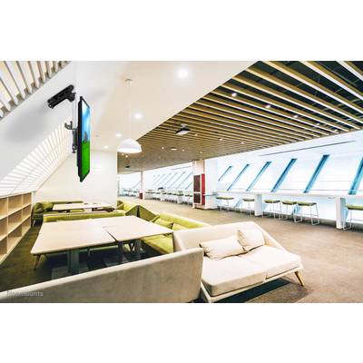 Egy modern, jól megvilágított loungeövezet zöld kanapékkal, asztalokkal és a falon lévő képernyővel. Fa gerendás mennyezet.