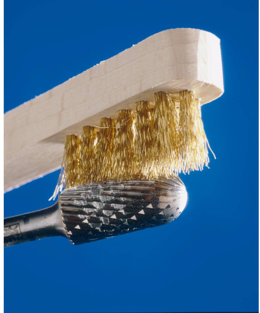 Egy drótkefébe húzott kefe tisztít egy marófúrót. A sörtéi sárgarézből vannak, és érintkeznek a fémes marófúróval kék háttér előtt.