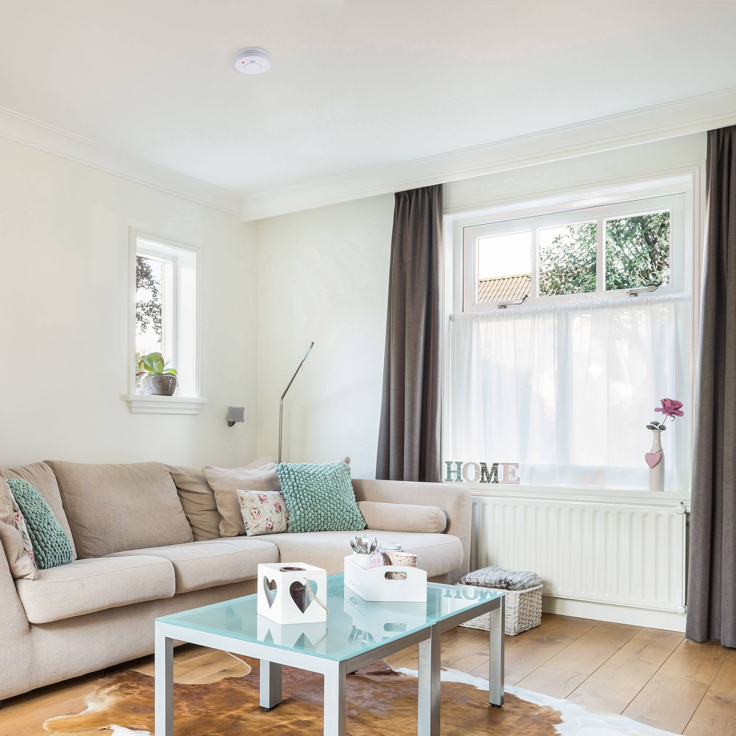 Világos nappali bézs kanapéval, kék párnákkal, szürke függönyökkel és egy dohányzóasztallal; ablak 'HOME' feliratú dekorációval.