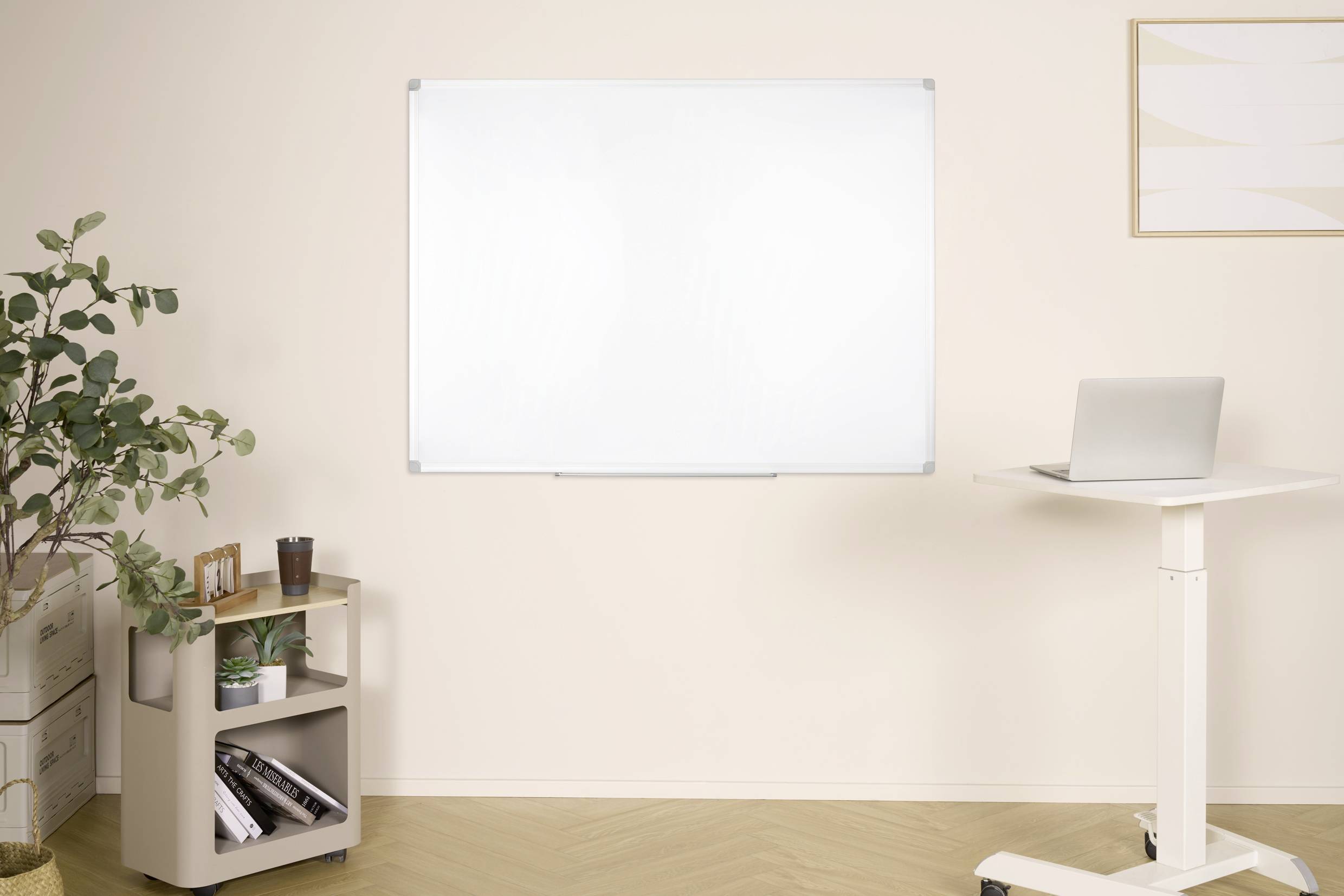 Egy iroda egy laptoppal egy állóasztalon, egy whiteboard a falon és egy polc könyvekkel és növényekkel.