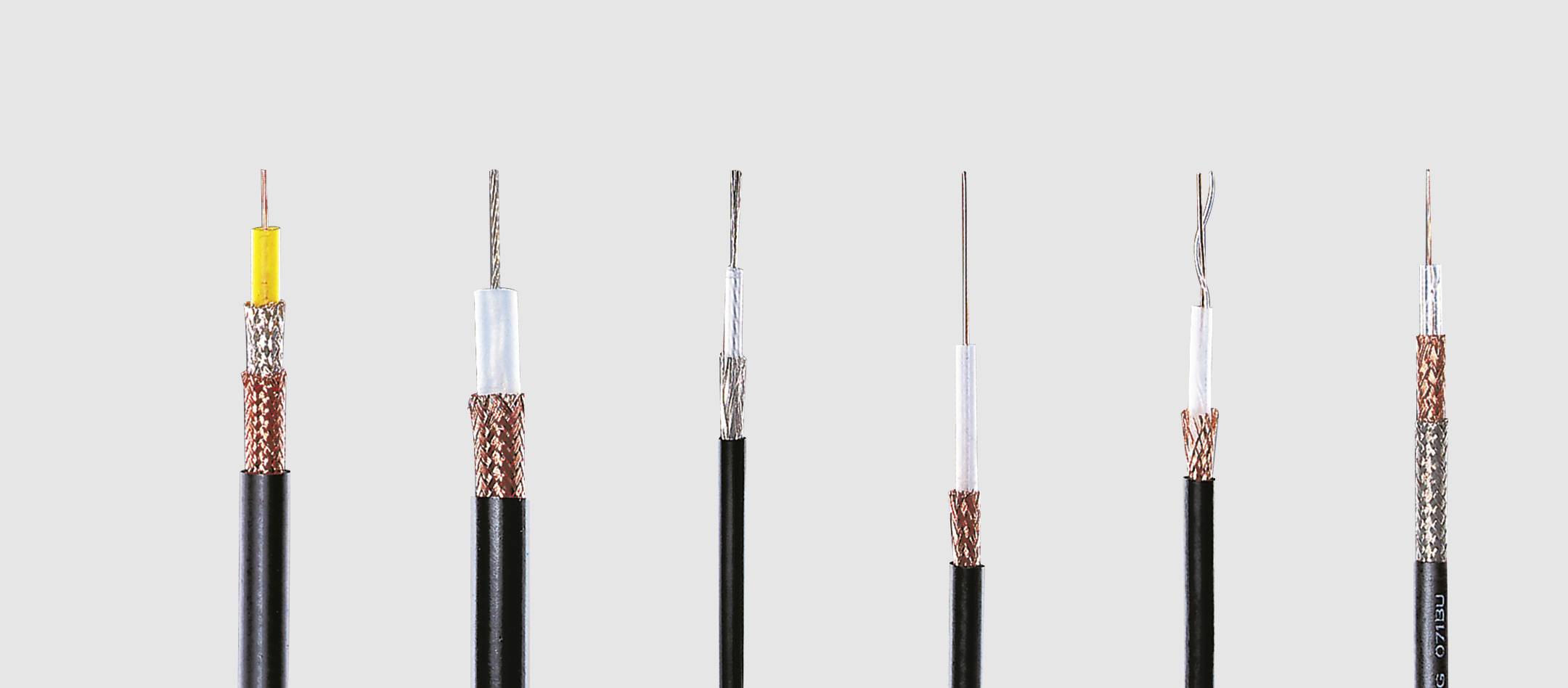 Több, különböző típusú és vastagságú koaxiális kábel sorakozik egymás mellett egy szürke háttér előtt.