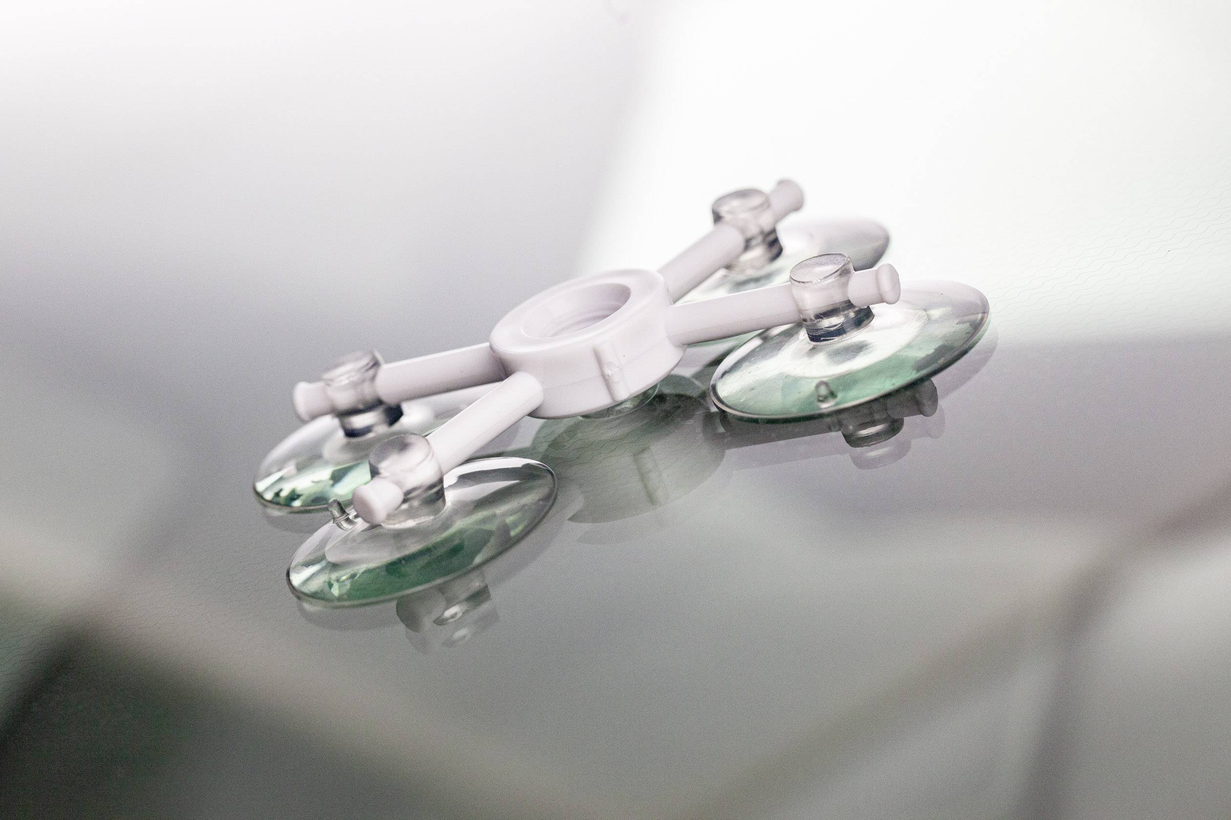 Egy fehér tapadókorongos eszköz négy zöld tapadókoronggal sima, fényvisszaverő felületen fekszik.