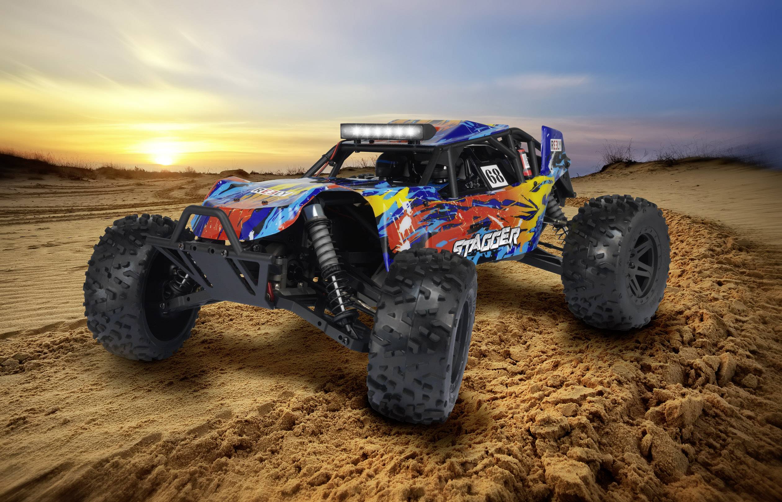 Egy távirányítású terepjármű tarka dizájnnal halad át egy homokos sivatagi tájon napnyugtakor.