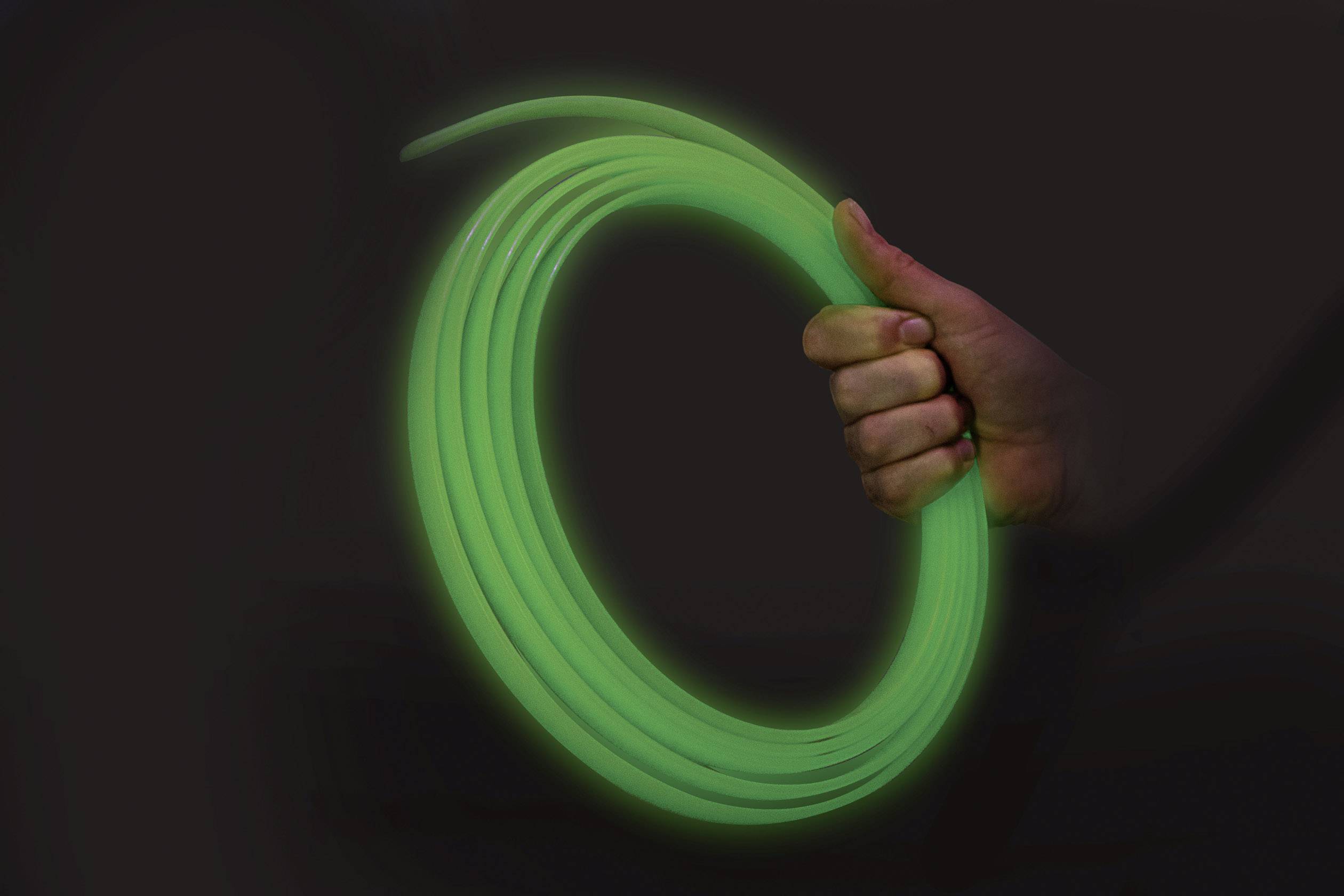 Egy kéz egy sötét háttérben egy élénkzöld tömlőt tart, amely az anyag fényességére utal.
