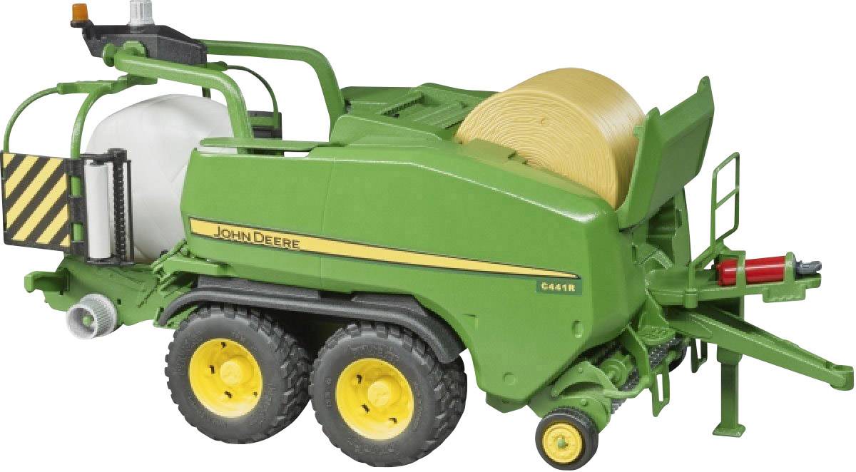 Zöld John Deere bálázógép sárga bálával, két kerékpárral, egy területen parkolva.