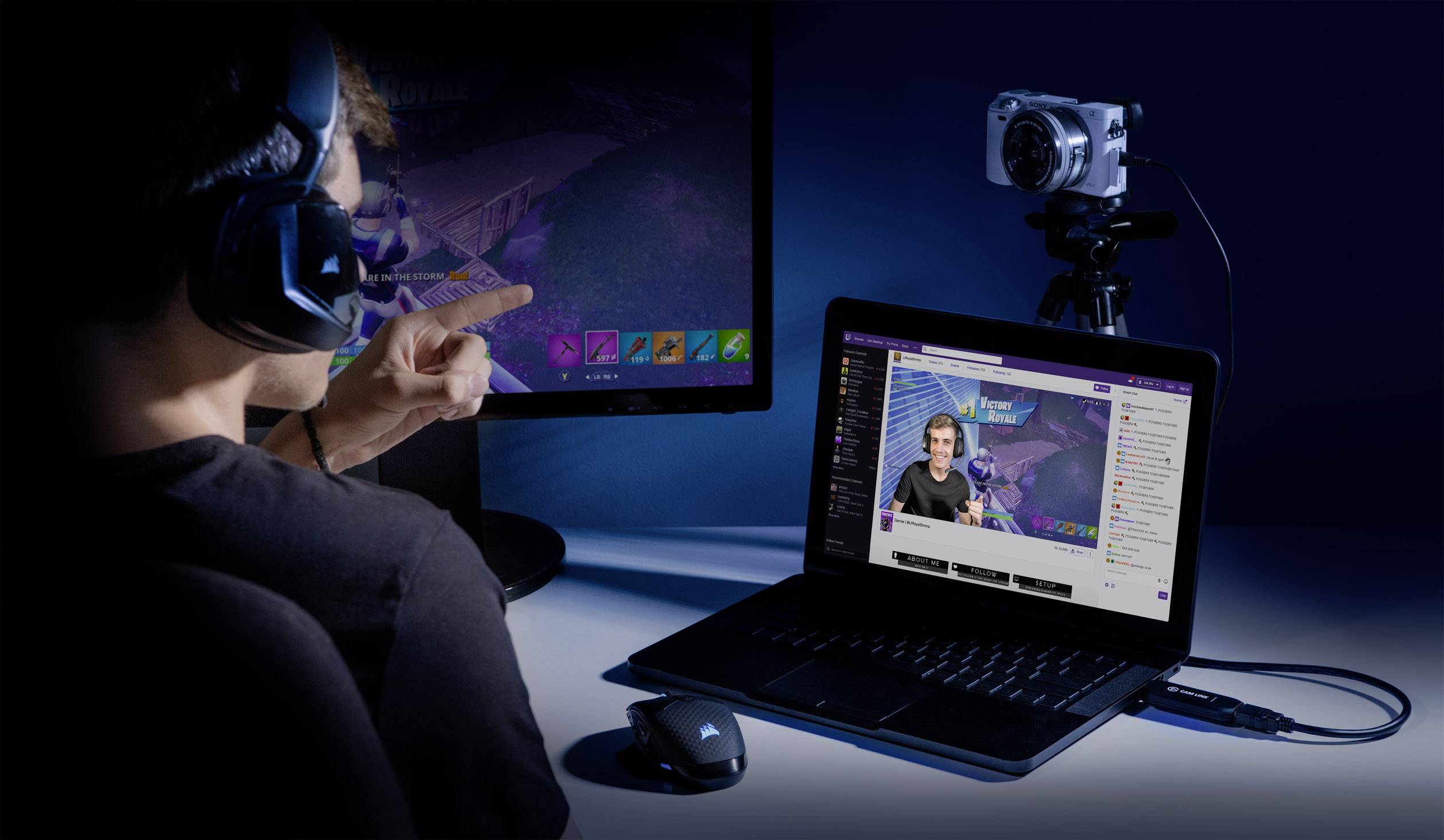 Egy fejhallgatós személy videójátékot közvetít. Egy laptopot és egy kamerát használ gameplay-je élő adásához. A háttérben egy monitor előtt fut a játék.