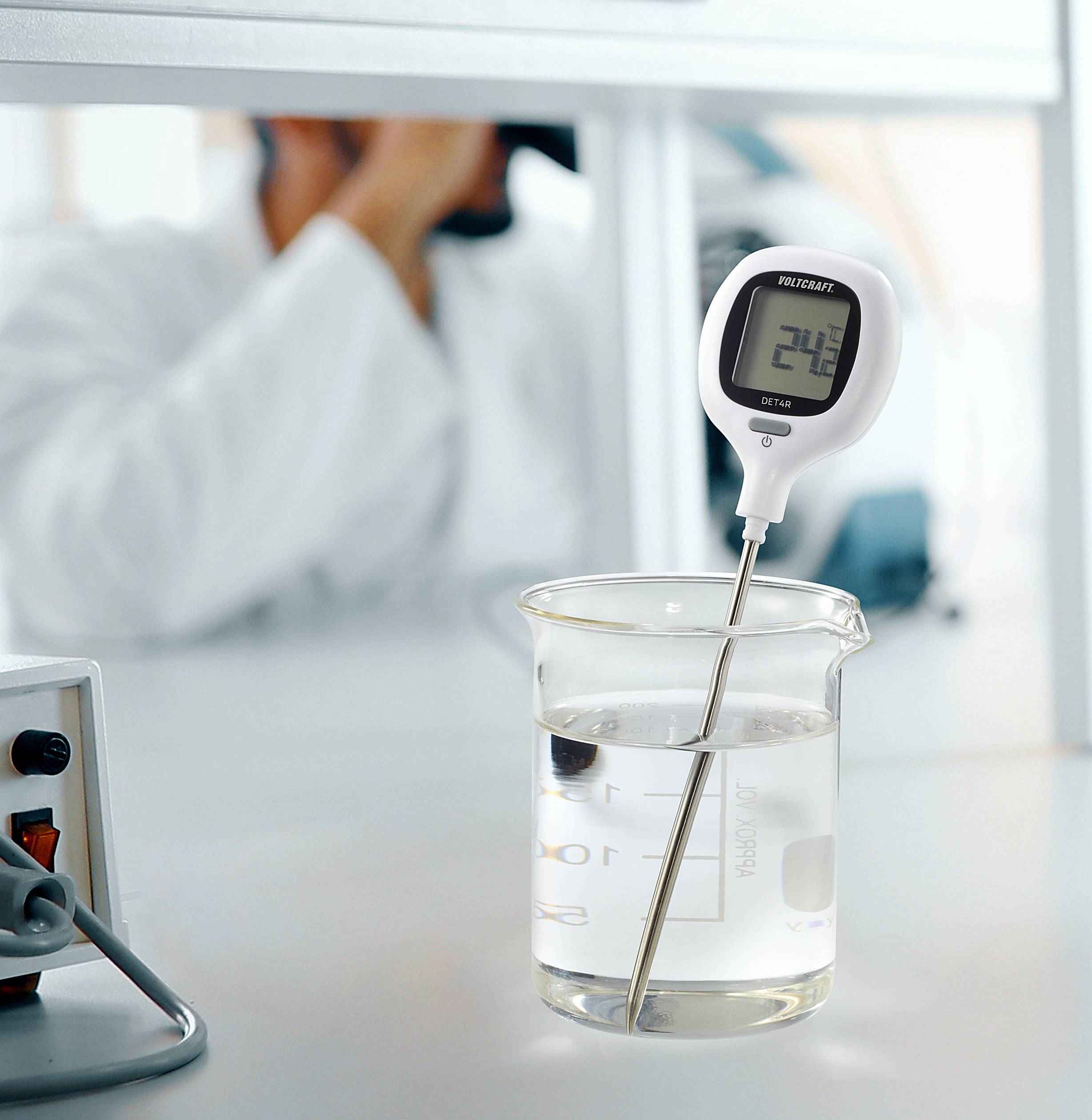 Egy digitális hőmérő 24,8 fokot mutat Celsius-skálán, miközben egy főzőpohárban lévő vízben áll. Laboratóriumi háttér látható.
