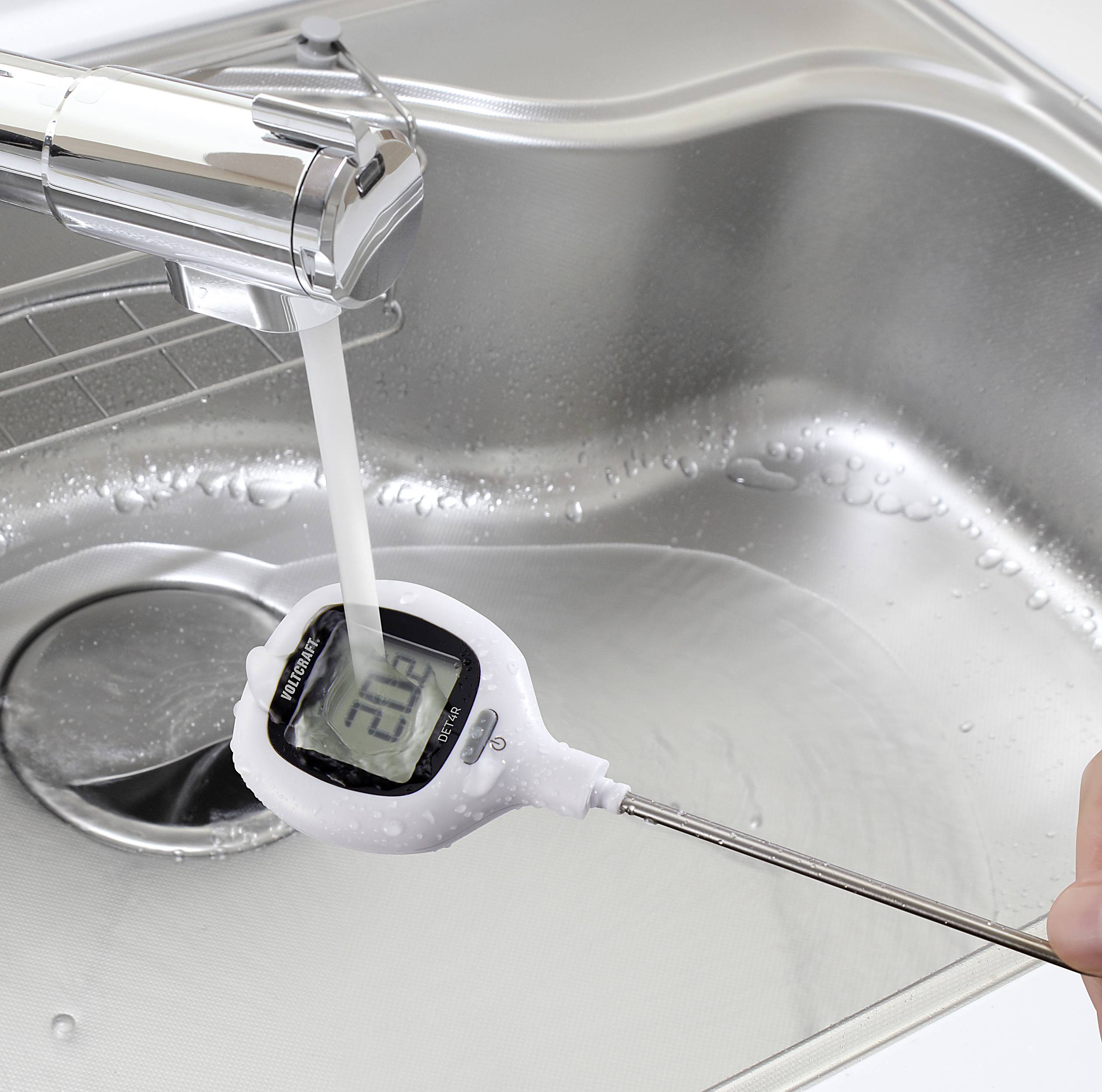 Egy digitális konyhai maghőmérő kijelzőjét folyó víz alatt öblítik le, hogy megtisztítsák. A mosogató rozsdamentes acélból készült.