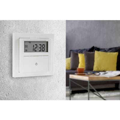Egy programozható fali óra '12:38' időpontot mutat. A háttérben egy modern nappali látható, benne egy kanapéval és egy asztallal.