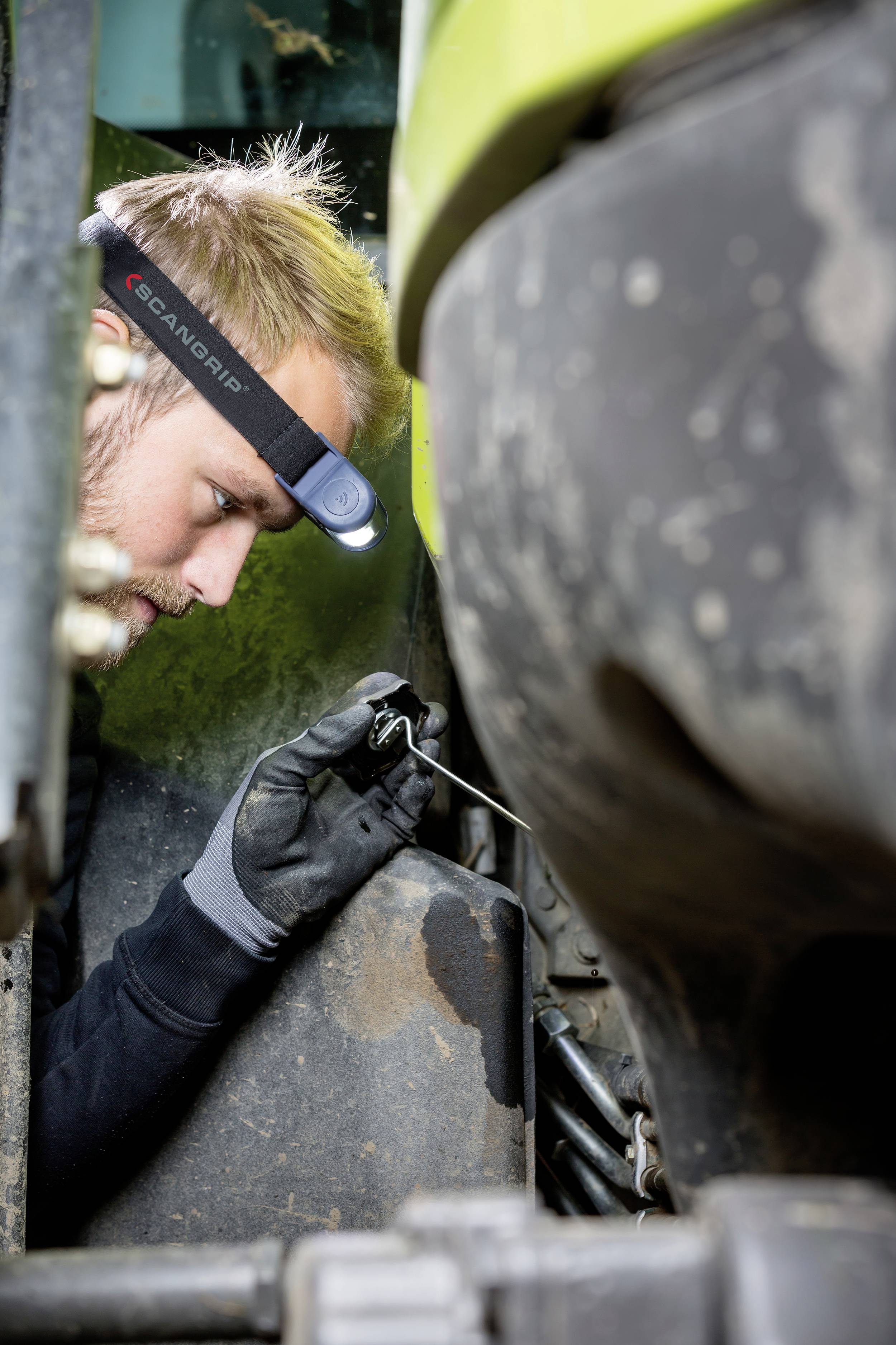 Egy férfi profilból, összpontosítva dolgozik egy gépteremben. Fejlámpát visel, és egy szerszámot tart a kezében.