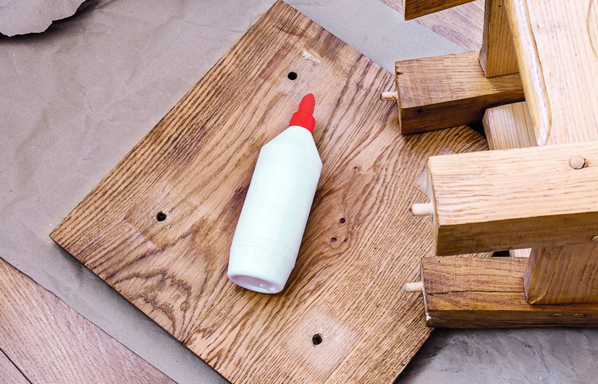 Fehér ragasztóburkú üveg piros szórófejjel egy fa deszkán, mellet egymásra rakott fa kockák.