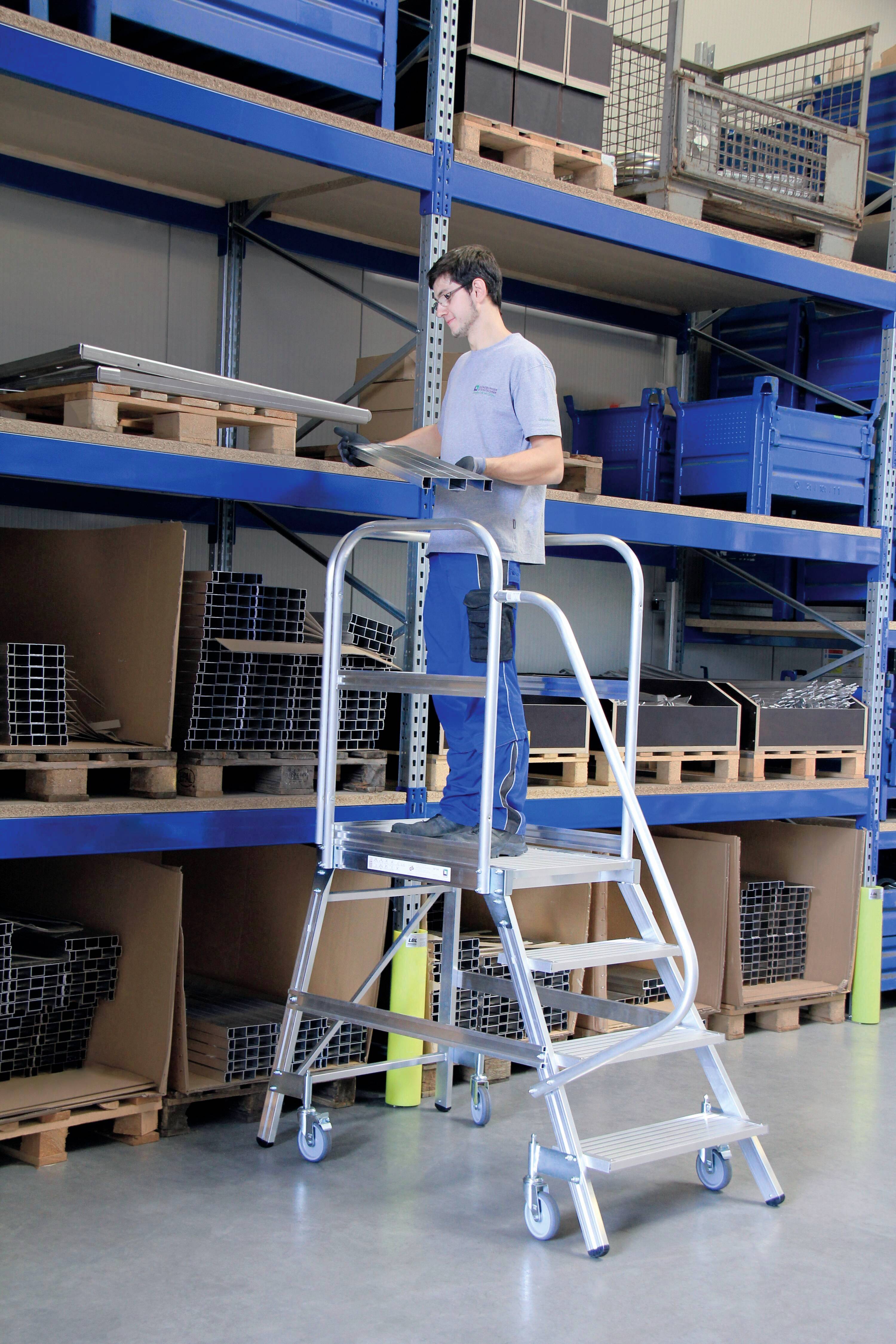 Egy személy egy stabil, korláttal ellátott létrán áll egy raktárban, és dobozokat rendez egy magas polcon.
