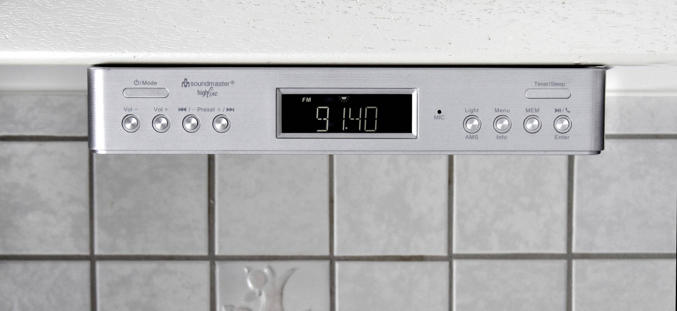 Digitális kijelzős autórádió, amelynek kijelzőjén az 'FM 91.4' felirat látható. Alatta kezelőgombok vannak a hangerő, csatornakeresés, óra és időzítő beállításához.