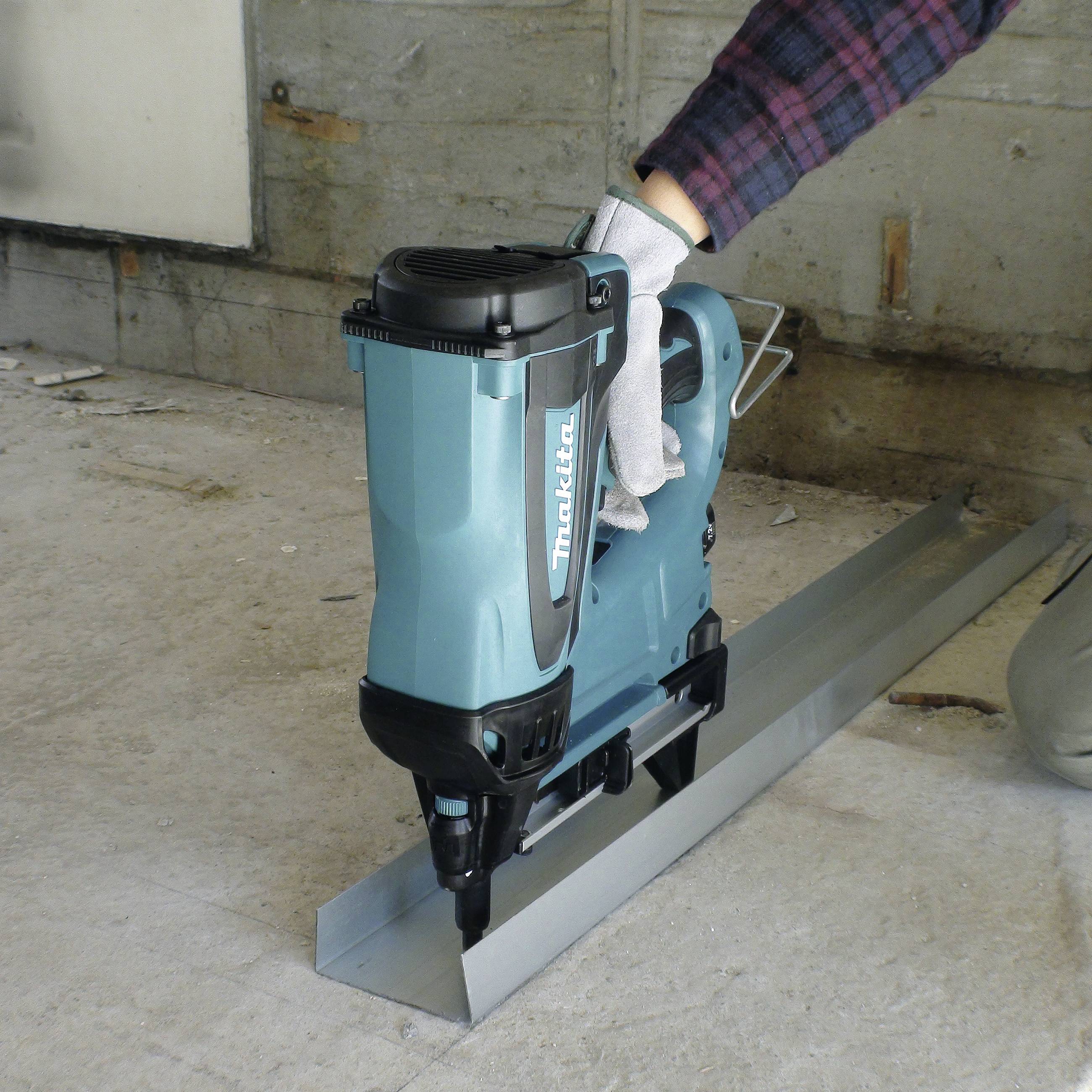 Egy személy egy türkiz színű vizsgálóeszközt tart egy fémdarab fölött egy épülőfélben lévő munkaterületen, a háttérben betonfalak láthatók.