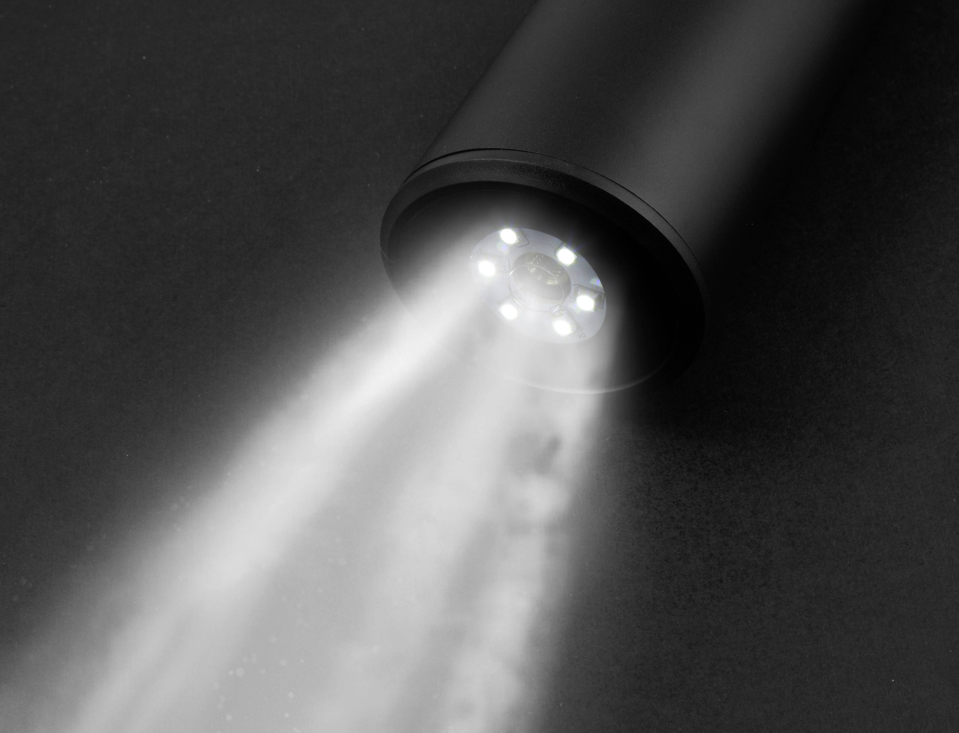 Közeli felvétel egy zseblámpáról, amint egy éles fénynyalábot vetít egy sötét felületre.