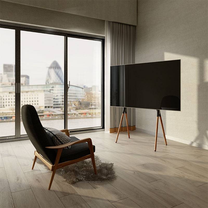 Szoba egy fekete fotellelés lapos képernyős tévével, fa padlóval, nagy ablakokkal, amelyekből kilátás nyílik a városra, modern épületek látszanak a háttérben.