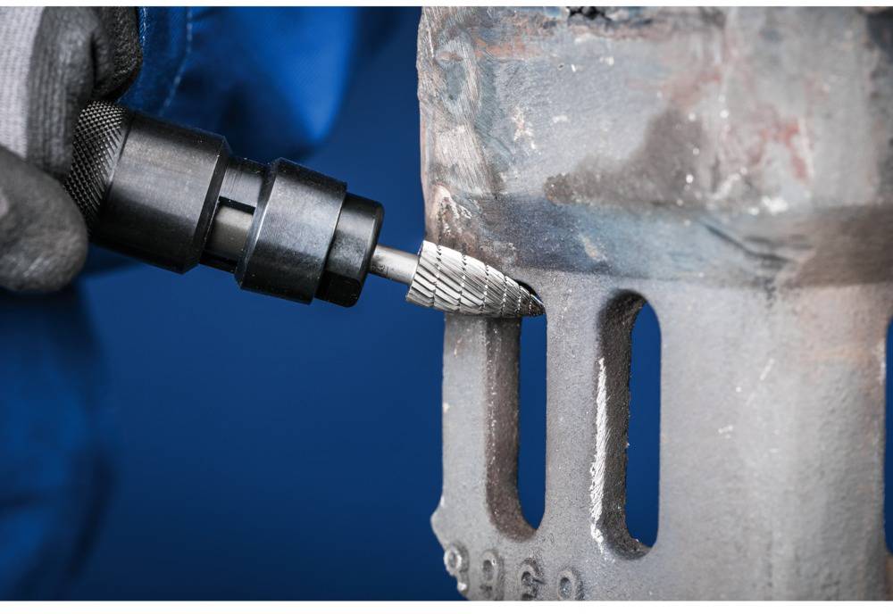 Egy személy egy fémfelületet munkál meg egy marófréssel. Kesztyűt és kék munkaruhát visel.