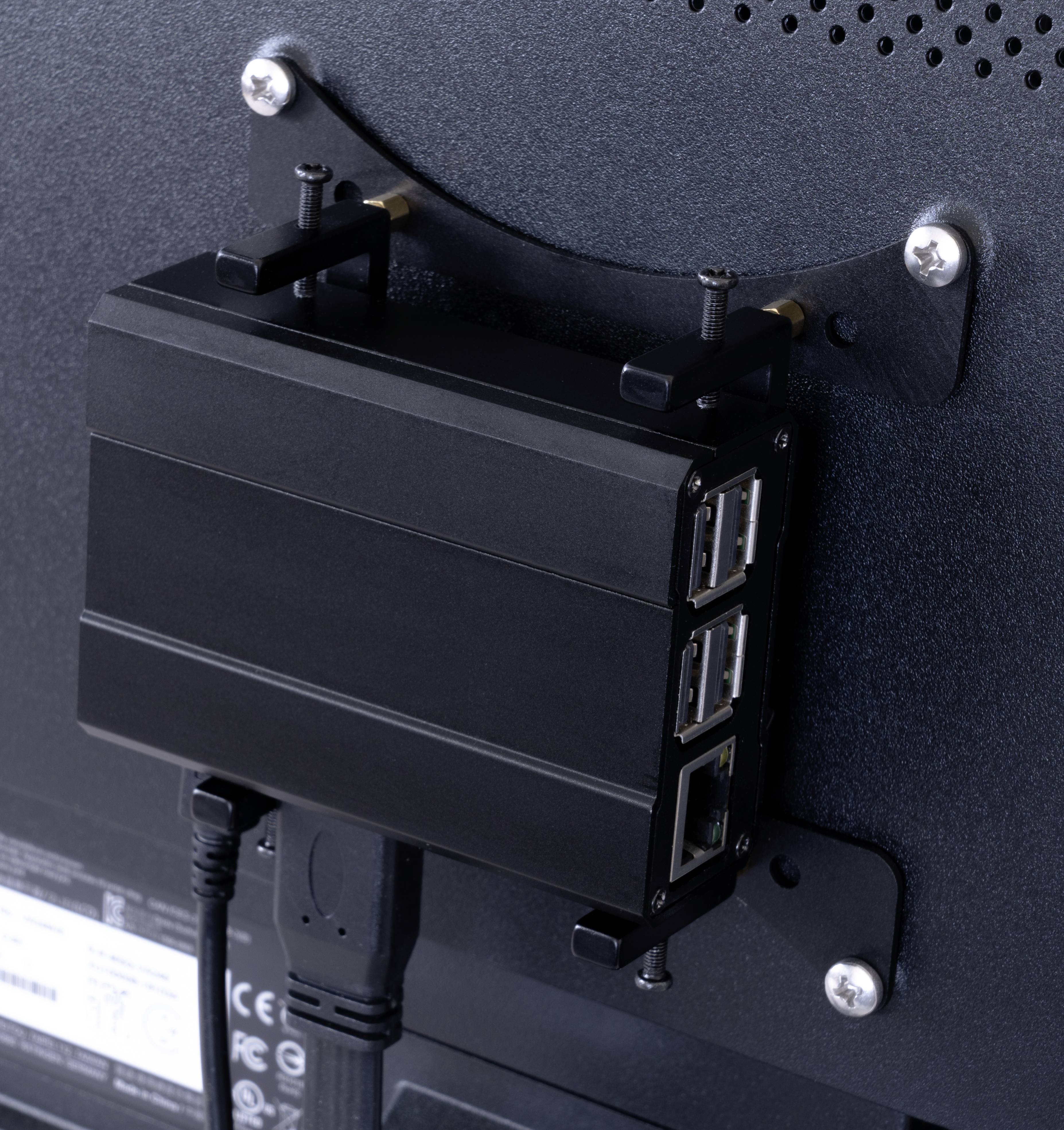 Egy kisméretű fekete számítógép több USB- és Ethernet-csatlakozóval egy monitor hátoldalára szerelve.