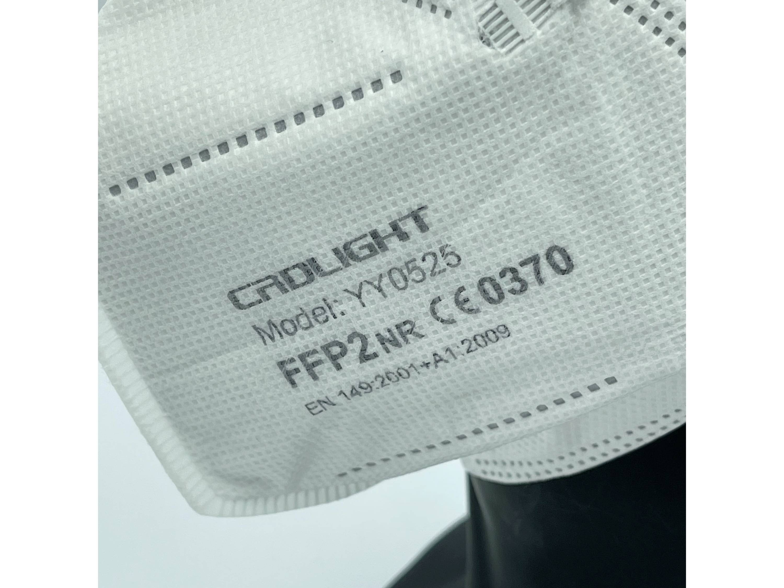 Egy FFP2-es maszk a „CRDLIGHT Model: XY0532 FFP2 NR CE 0370 EN 149:2001+A1:2009" felirattal, sötét felületen elhelyezve.