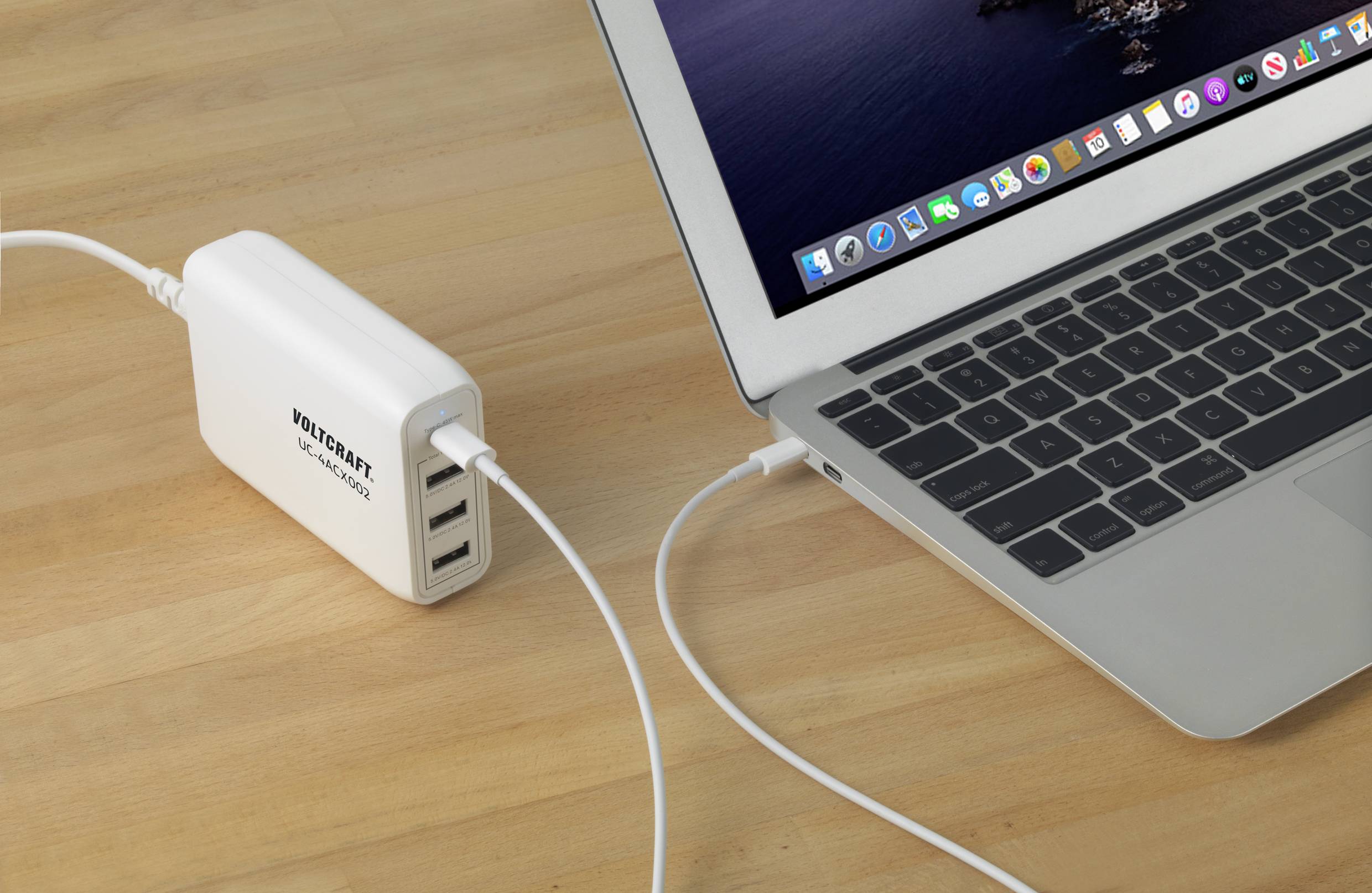 Egy laptop USB-töltővel kap áramot. A töltő több csatlakozóval rendelkezik, és egy fa asztalon helyezkedik el.