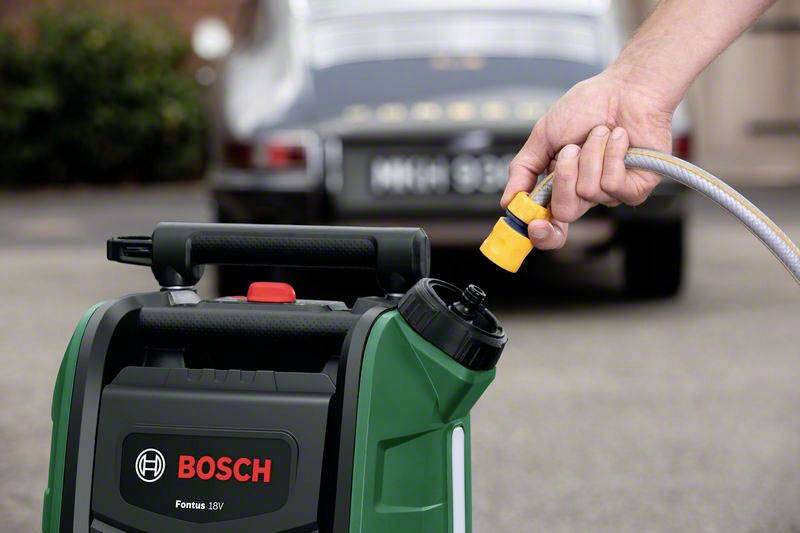 Egy hordozható Bosch magasnyomású mosó vízcsatlakoztatva van. A háttérben egy autó áll egy felhajtón.