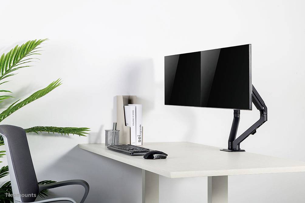 Modern íróasztal egy mozgatható karon lévő monitorral, billentyűzettel és egérrel. Baloldalon egy cserepes növény és egy irodai szék.