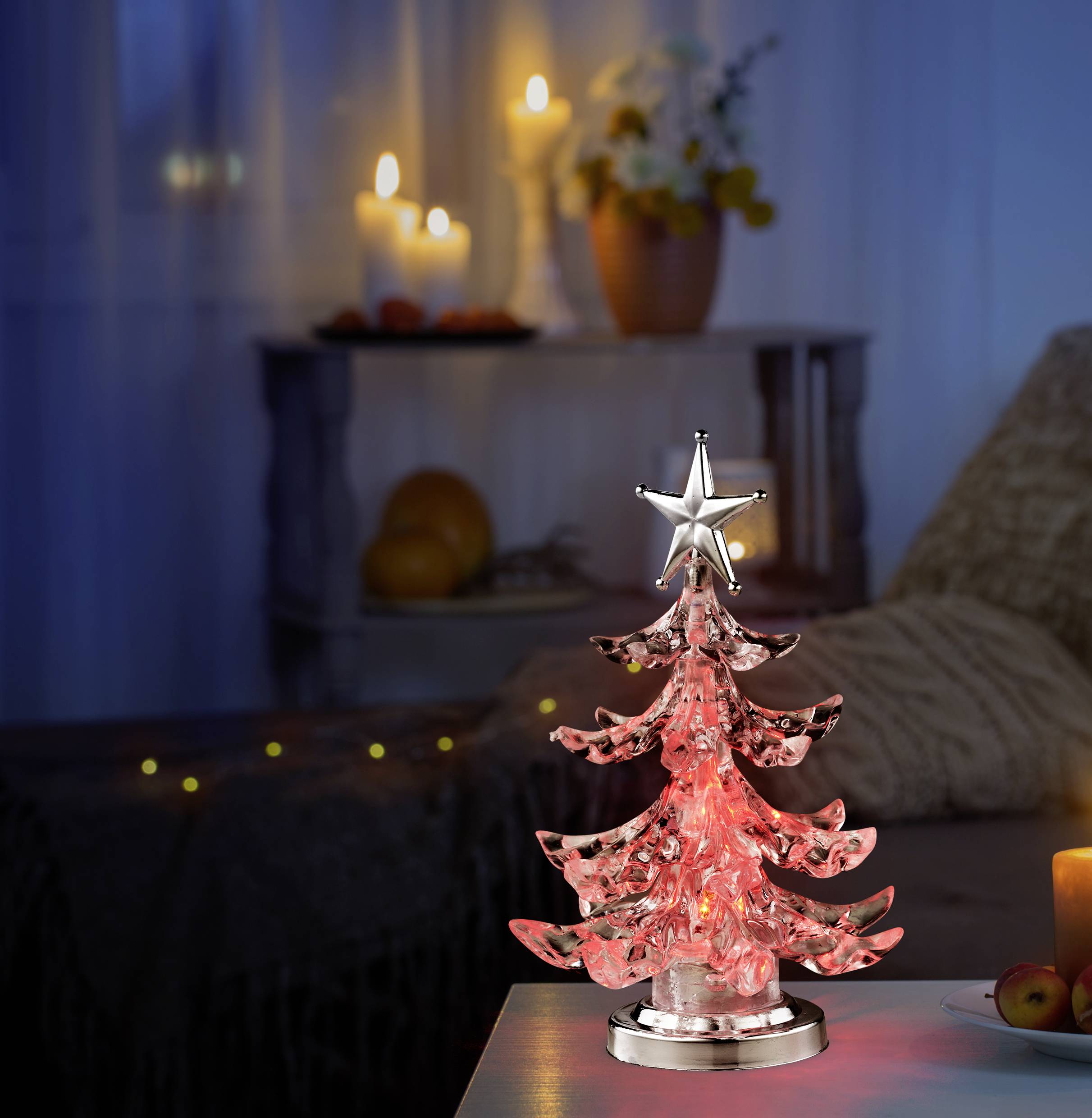 Ragyogó, rózsaszínű karácsonyfadísz csillag csúcsdísszel egy asztalon, egy hangulatosan megvilágított szobában gyertyákkal.