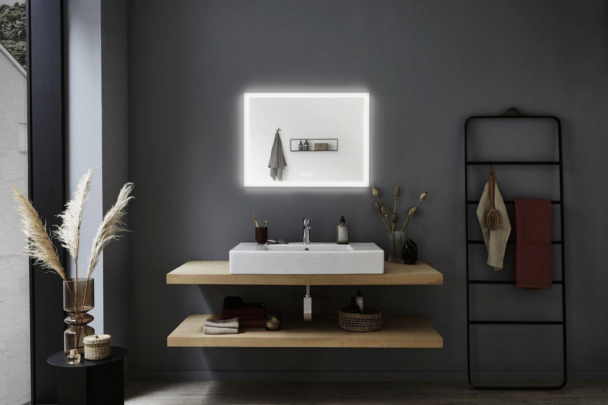 Modern fürdőszoba világító tükörrel, egy fapolcon elhelyezett mosdókagyló felett, szárított füvekkel díszítve és törölközőtartóval.