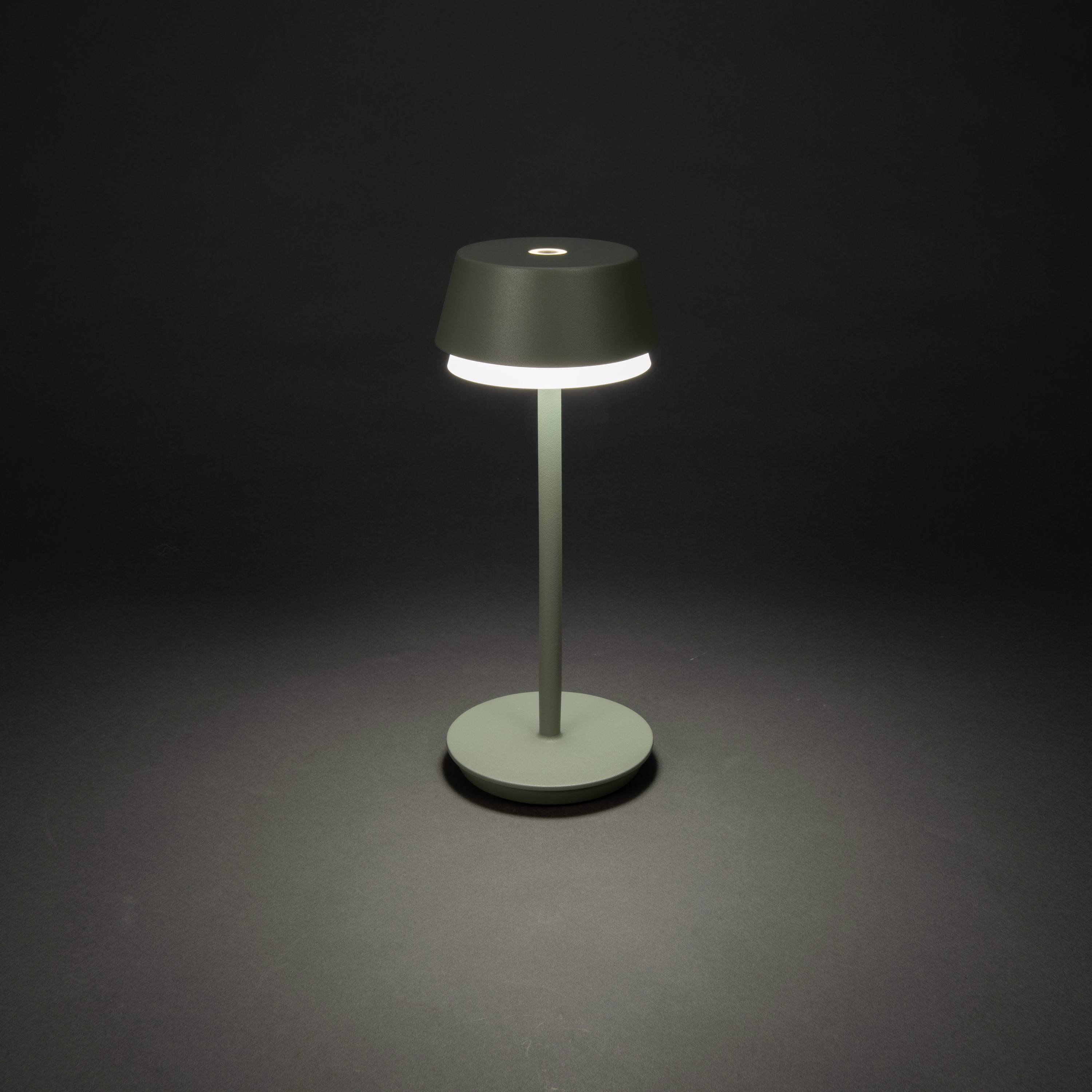 Egy modern, minimalista asztali lámpa egyszerű, hengeres talpazattal és kerek búrával, sötét háttér előtt világít.