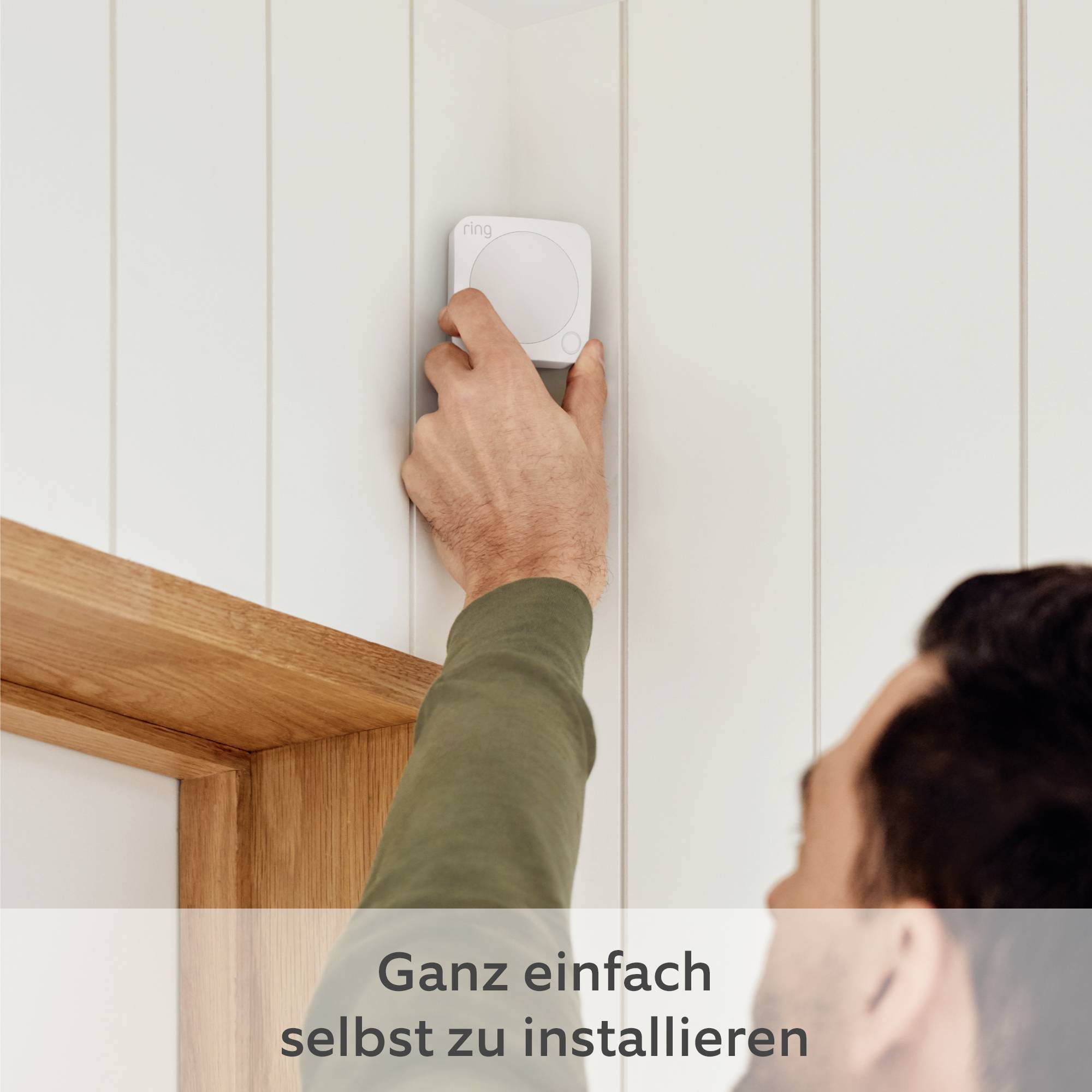 Egy személy egy kis fehér eszközt szerel fel a fal egy ajtó feletti részére, amelynek felirata alatt az áll: 'Egyszerűen saját kezűleg felszerelhető'.