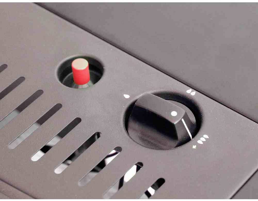 Egy fekete forgógomb egy fémeszköz oldalán, egy piros kapcsoló mellett, egy szellőzőnyílásokkal ellátott házban.