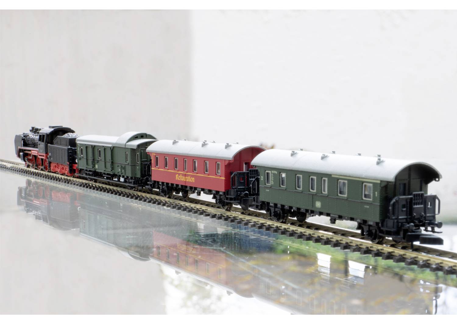 Egy modellvonat gőzmozdonnyal és négy kocsival egy sínpályán. Két kocsi zöld, egy piros, rajta a 'Märklin' felirattal.