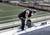 Egy személy egy üres stadionban dolgozik, miközben védőfelszerelést visel és egy fúrógépet használ.