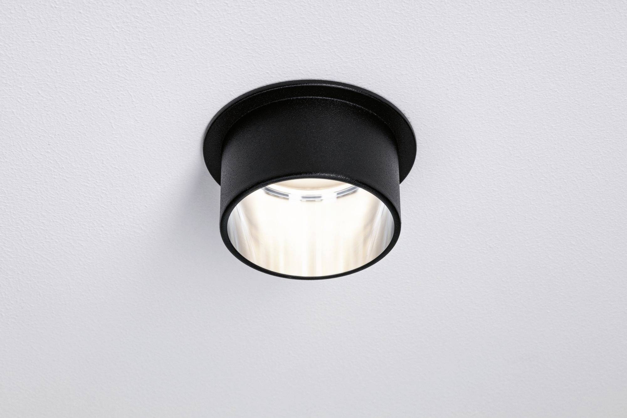 Egy fekete fém mennyezeti lámpa lágy, meleg fehér fényt sugároz. Formatervezése minimalistikus és modern.