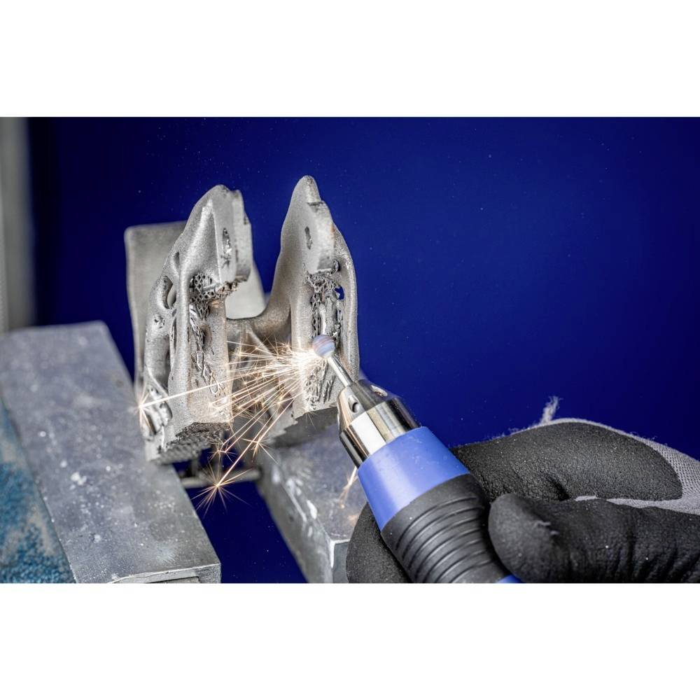 Egy személy forgó szerszámmal csiszolja a fémet. Szikrák pattannak le a fémről. A szerszámnak kék fogantyúja van.