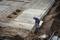 Munkás betonalap méreteit méri az épülő munkaterületen. A talaj helyenként nyitott, acélmerevítések láthatóak. Előkészületek a következő építési szakaszhoz.