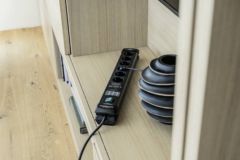 Elosztó több aljzattal egy fa polcon egy váza mellett.