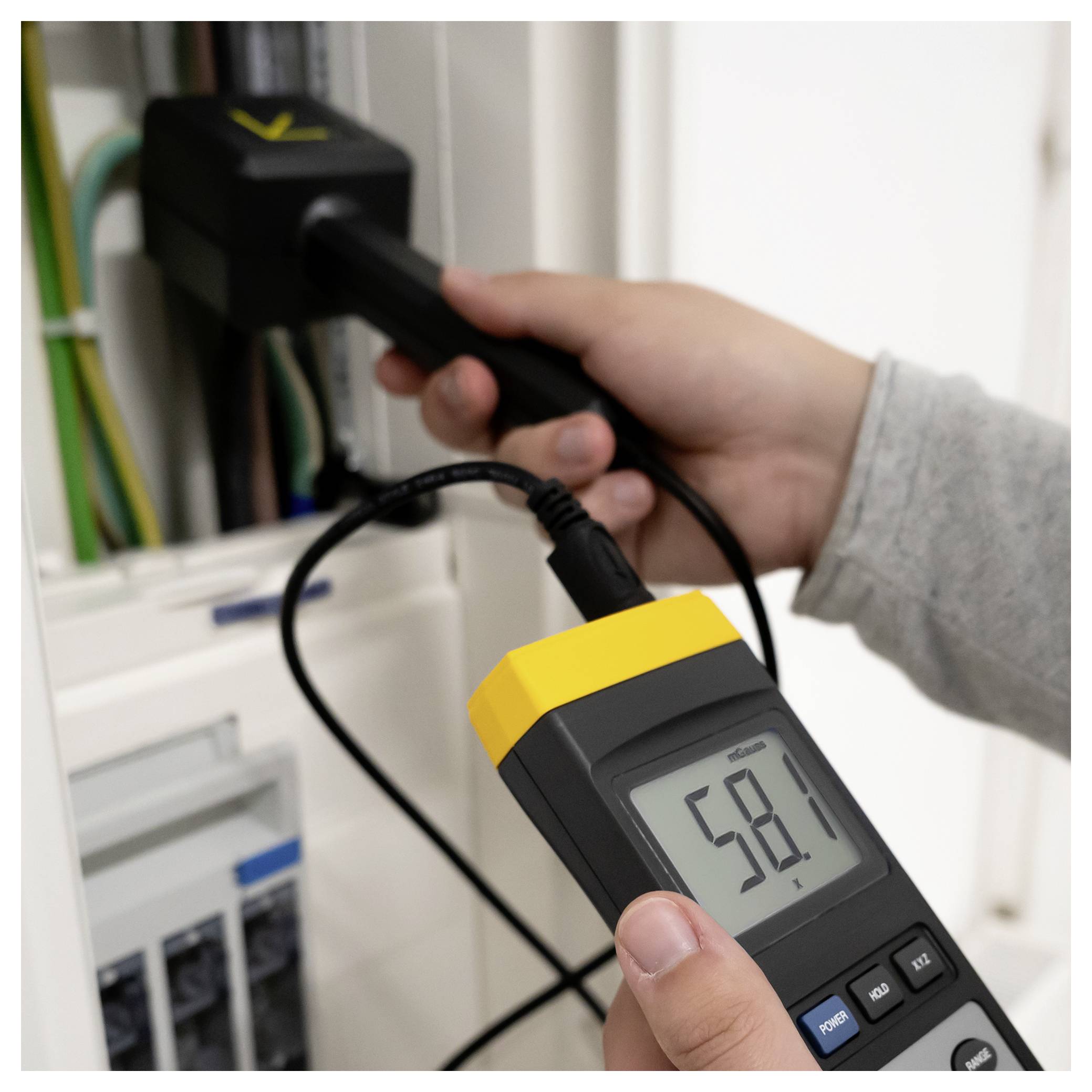 Az egyik személy egy beépített elektromos teszterrel mér egy csatlakoztatott elektromos aljzatot, amely 58,1 voltos értéket mutat.