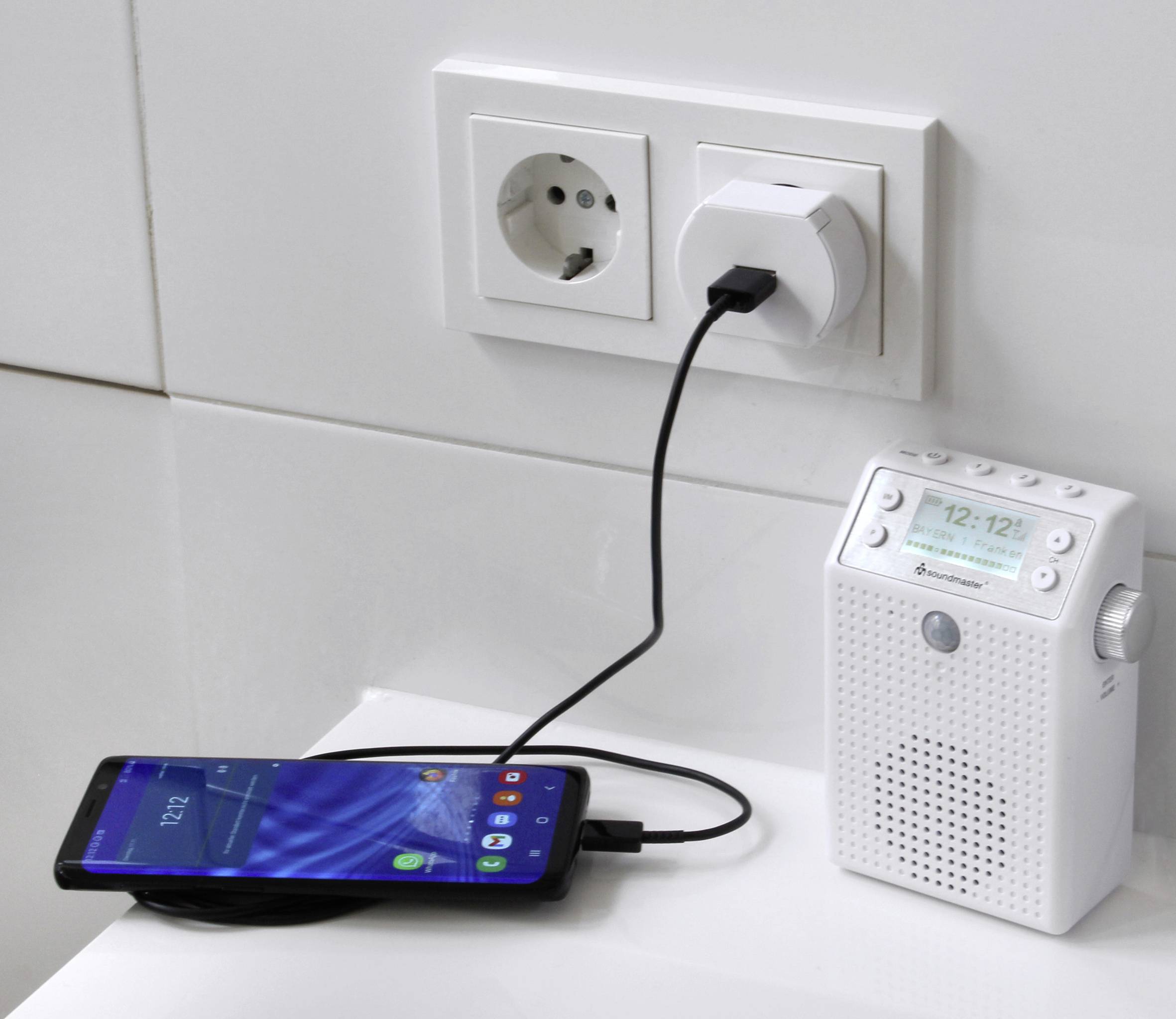 Egy okostelefon USB-kábel segítségével csatlakozik egy hálózati aljzatba dugható rádióhoz, amely maga is csatlakoztatva van egy elektromos aljzathoz.