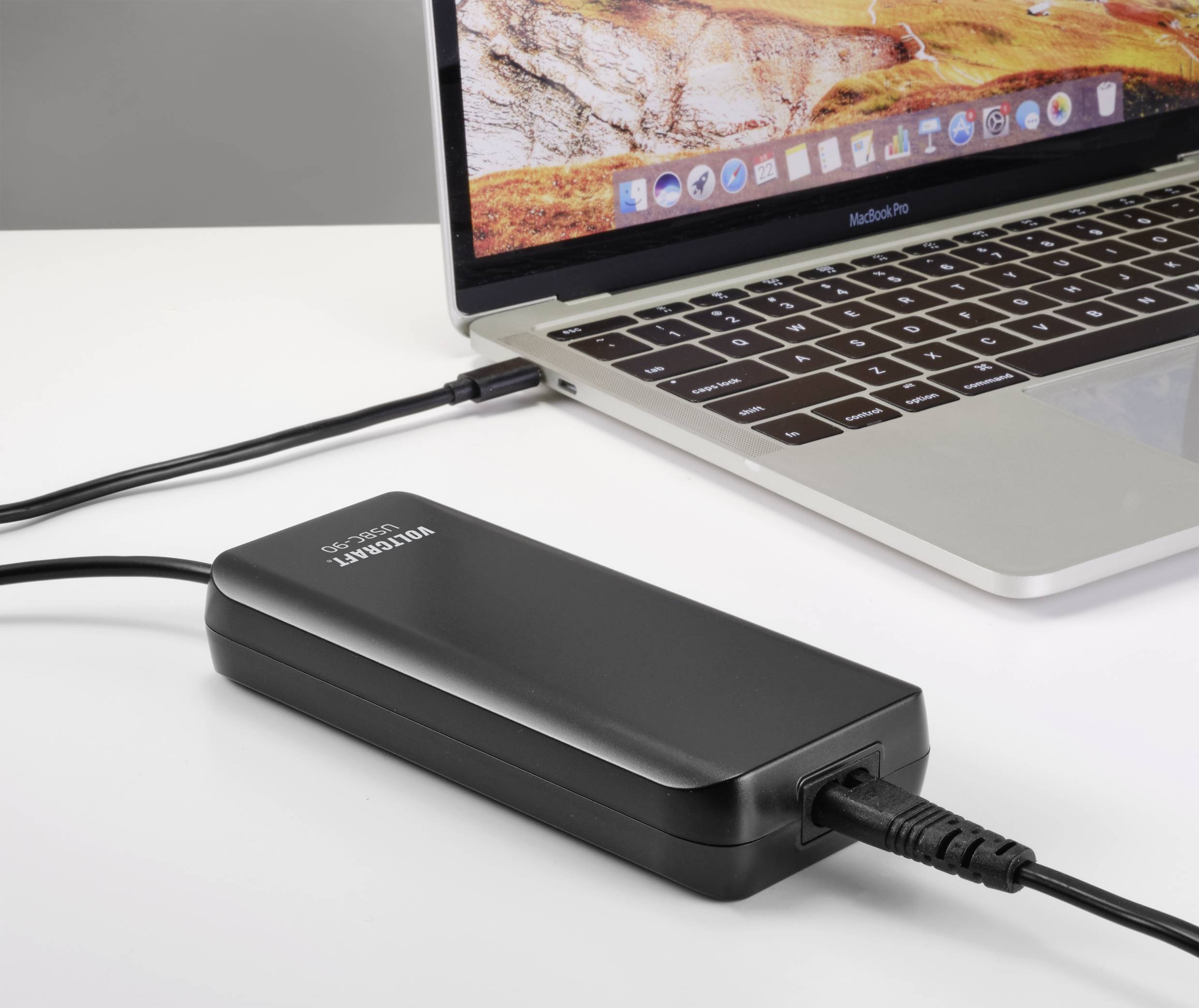 Egy laptop egy USB-kábelen keresztül tölt egy powerbank segítségével. A laptop képernyőjén egy tájkép látható.