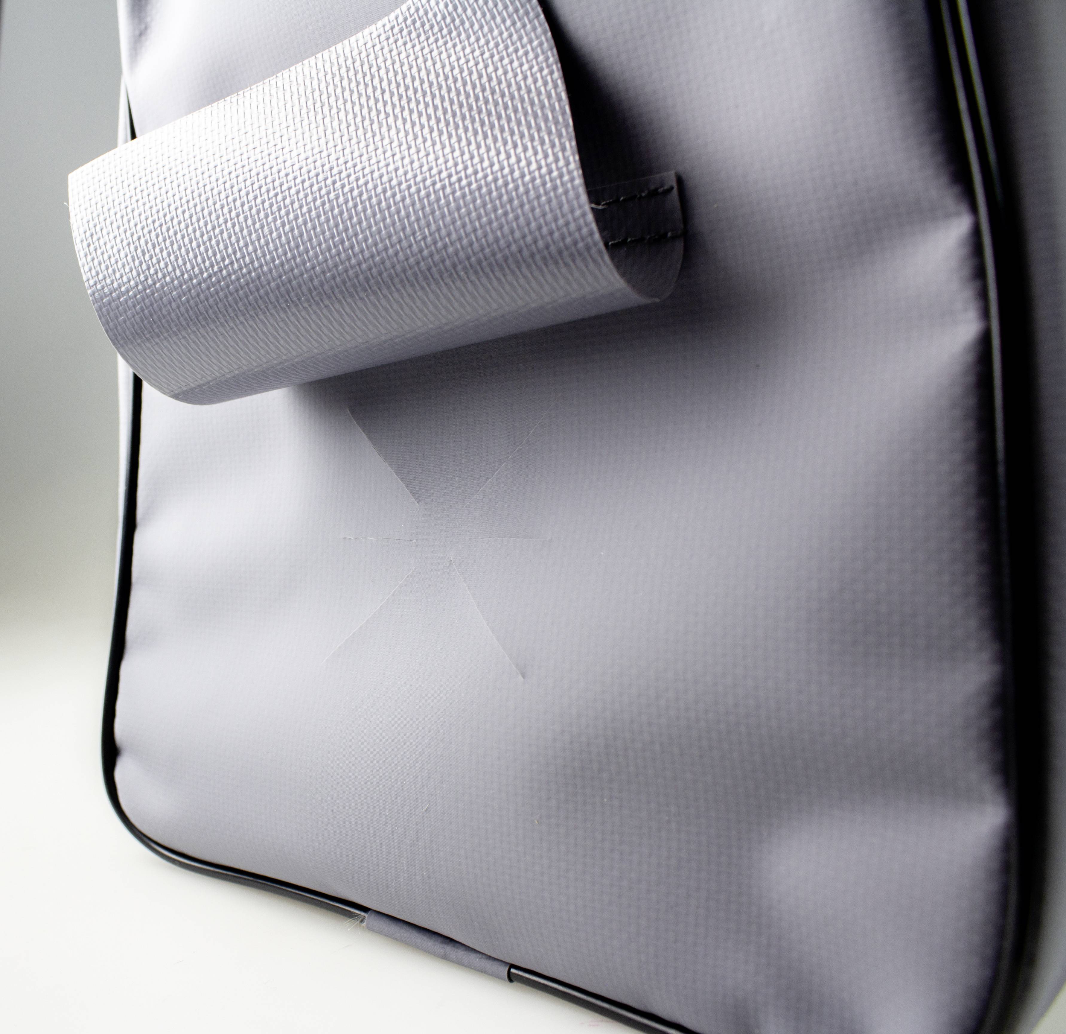 Egy szürke anyagú táska vékony szerkezettel. Egy patentos záródás látható. A felülete vízlepergető hatású.