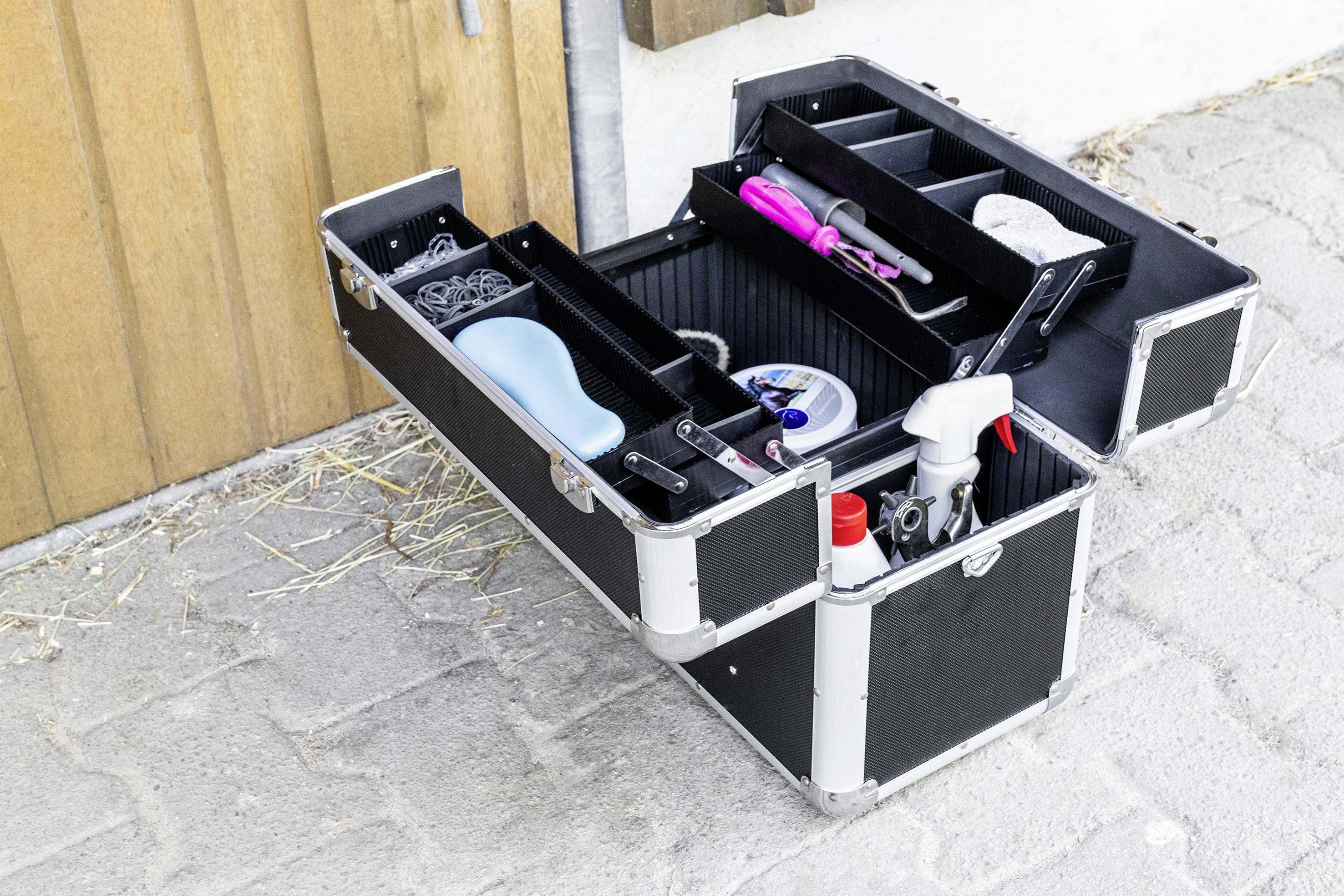 Nyitott fodrász táska a padlón, benne különféle eszközökkel, mint fésű, kefe és ápolósprayék.