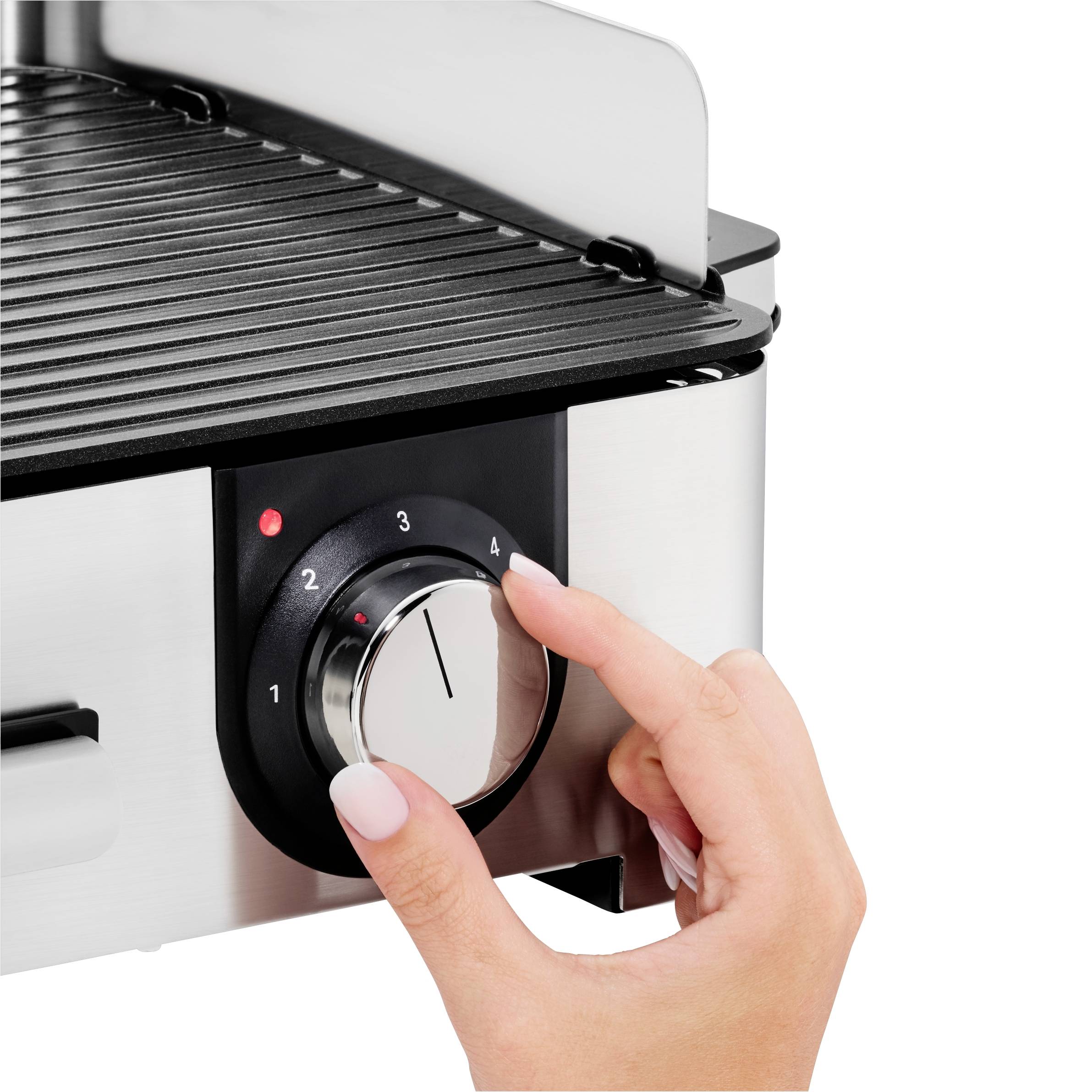 Egy kéz elfordítja egy elektromos grill hőmérséklet-szabályzóját, 4-es fokozatra állítva. A grillnek sötét főzőfelülete van.