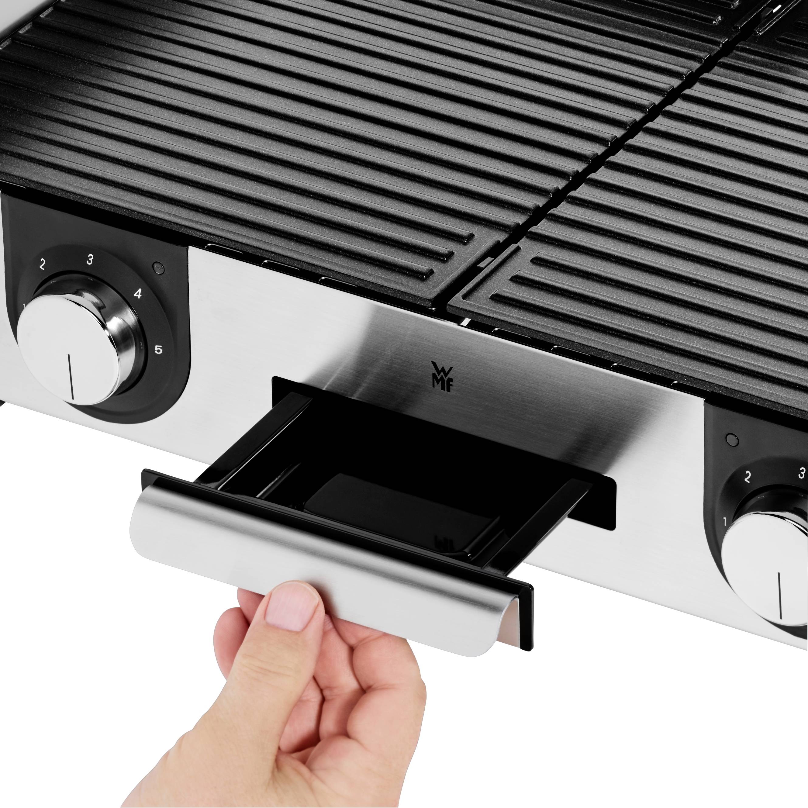 Egy kéz kihúz egy fiókot egy elektromos grillből. A grill rozsdamentes acélból készült, és szabályzók vannak az elején.
