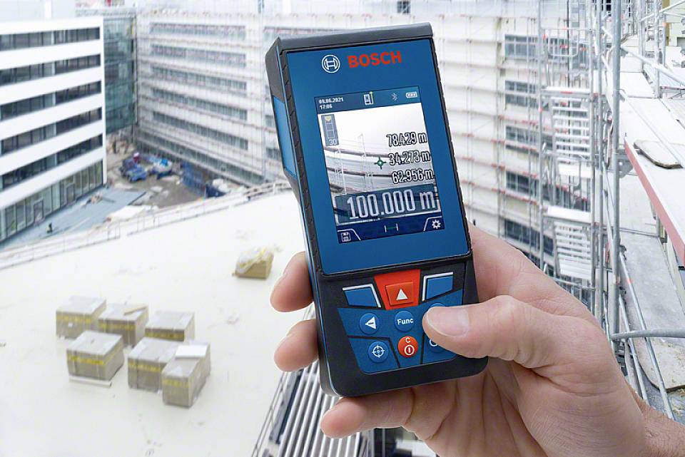 Egy személy egy digitális lézer távolságmérővel 100.000 méter távolságot mér egy építkezésen.