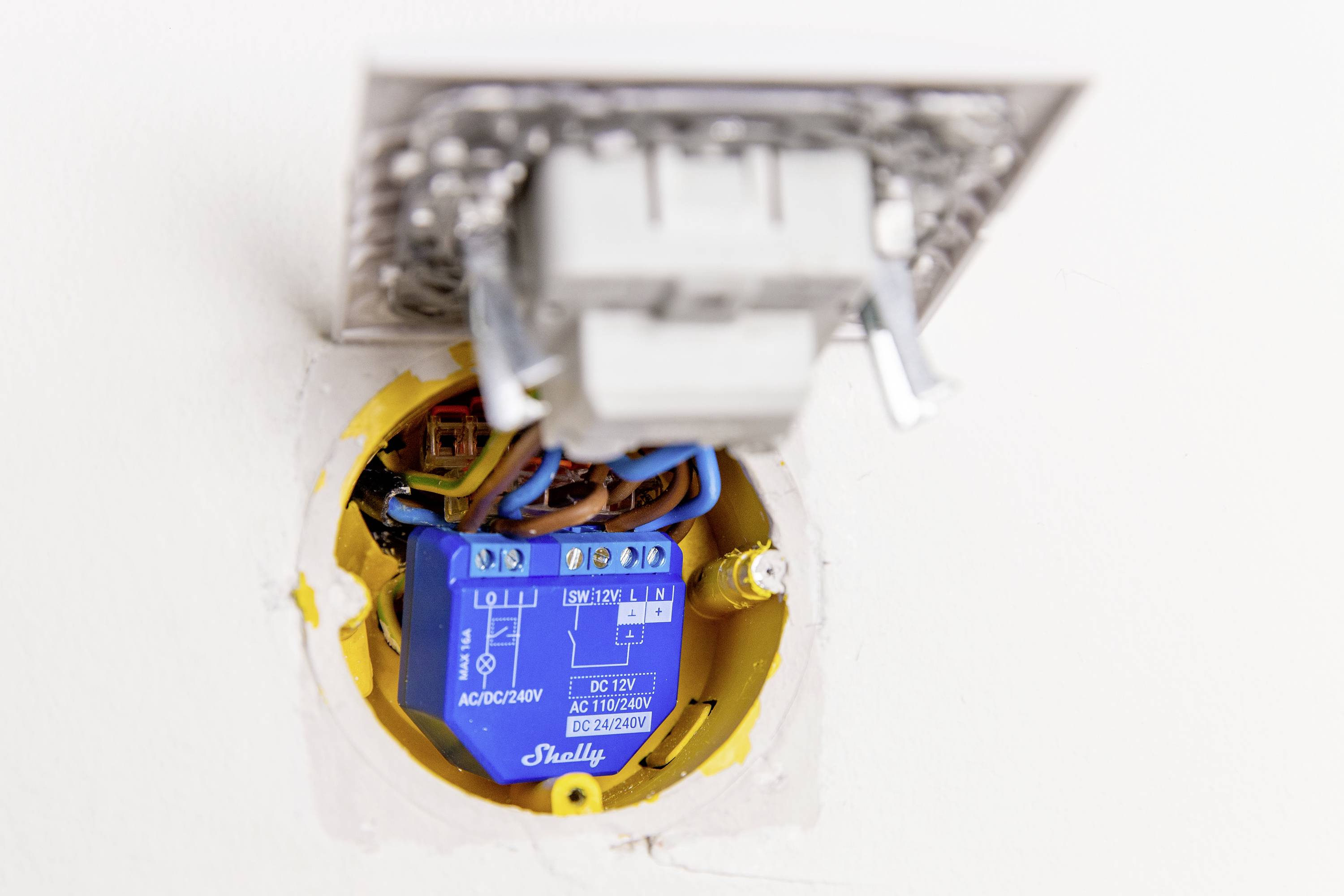 Egy nyitott fali kapcsoló egy beépített kék relét mutat elektromos kábelekkel.