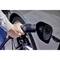Egy személy egy elektromos járművet tölt azáltal, hogy a töltőcsatlakozót egy autó töltőaljzatába dugja.