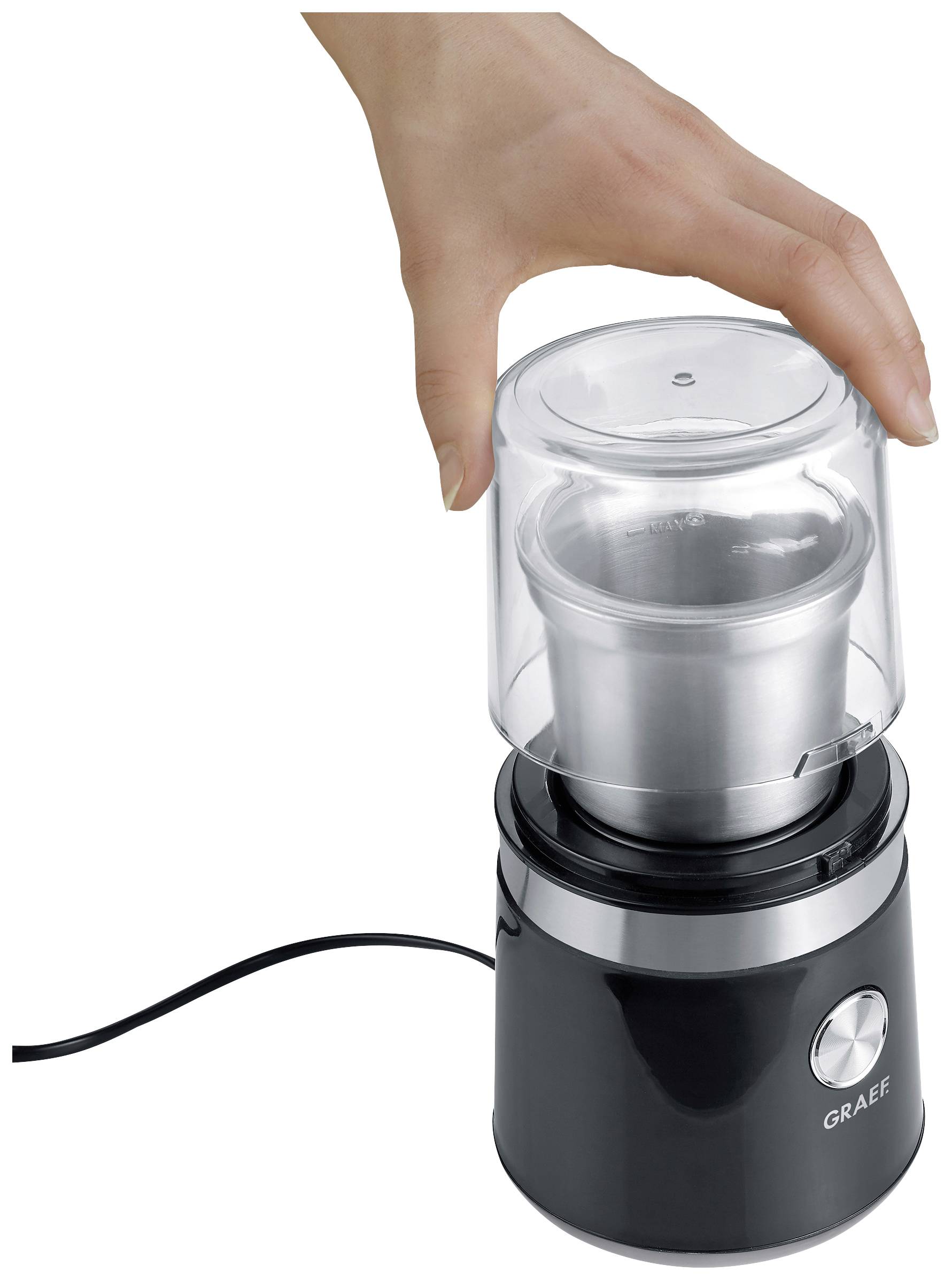 Egy kéz egy fekete elektromos kávédarálót forgat, amelynek átlátszó fedele van fehér háttér előtt.